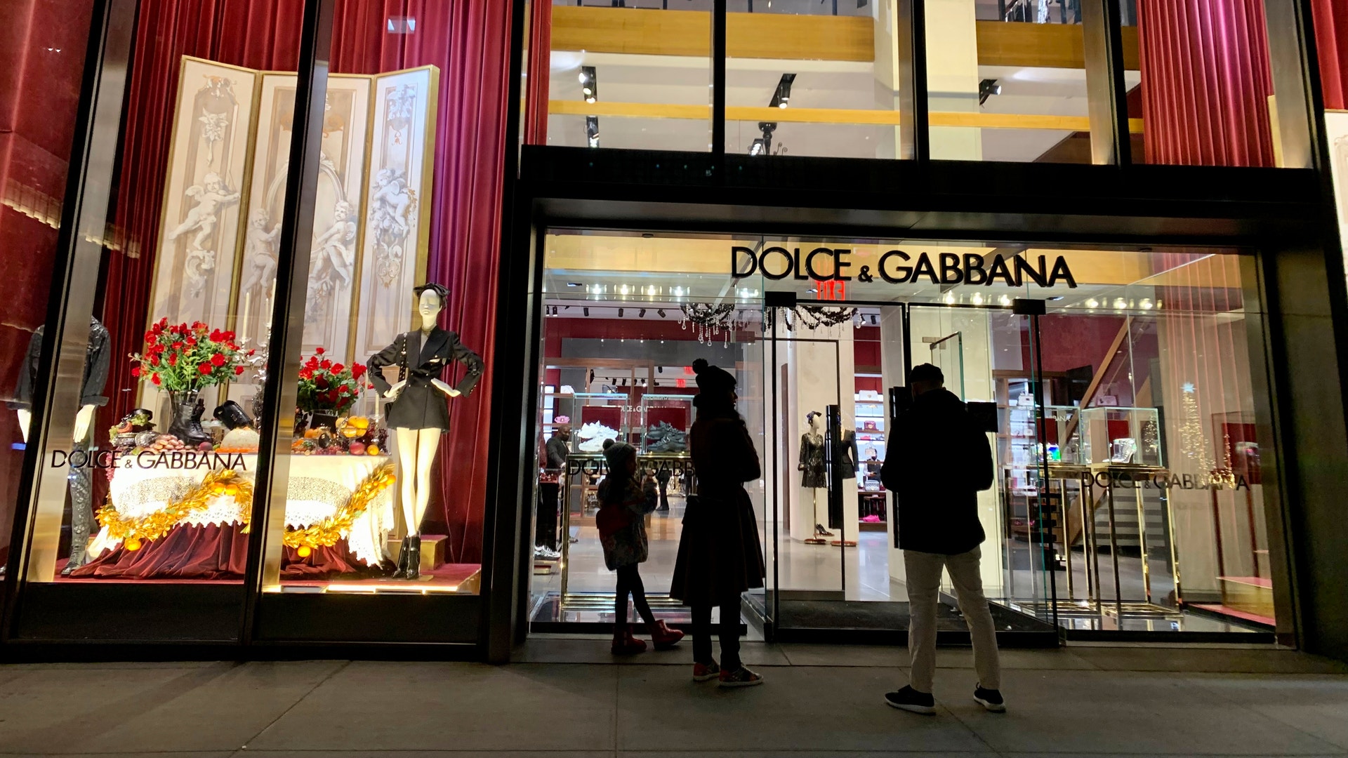 Butiksfasad för Dolce & Gabbana med röda vertikala lameller, stora skyltfönster och människor som går förbi på gatan.