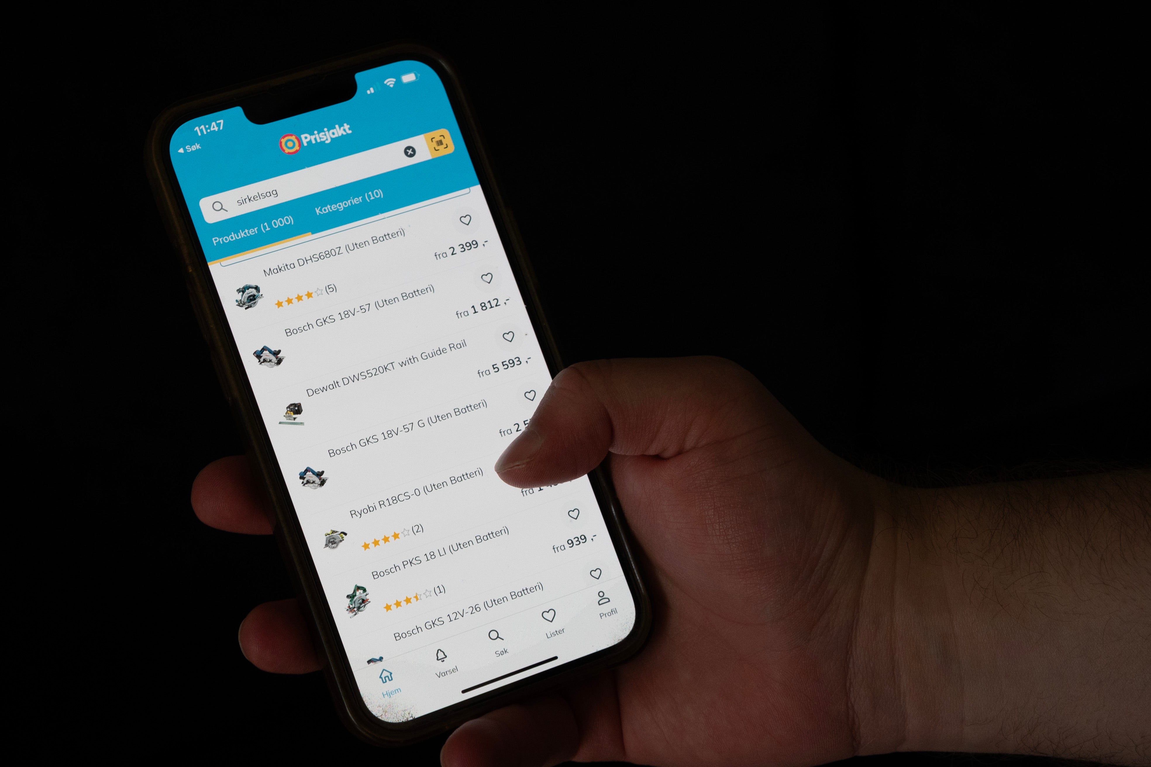En hand håller en mobiltelefon som visar Prisjakts app med en lista över produkter.