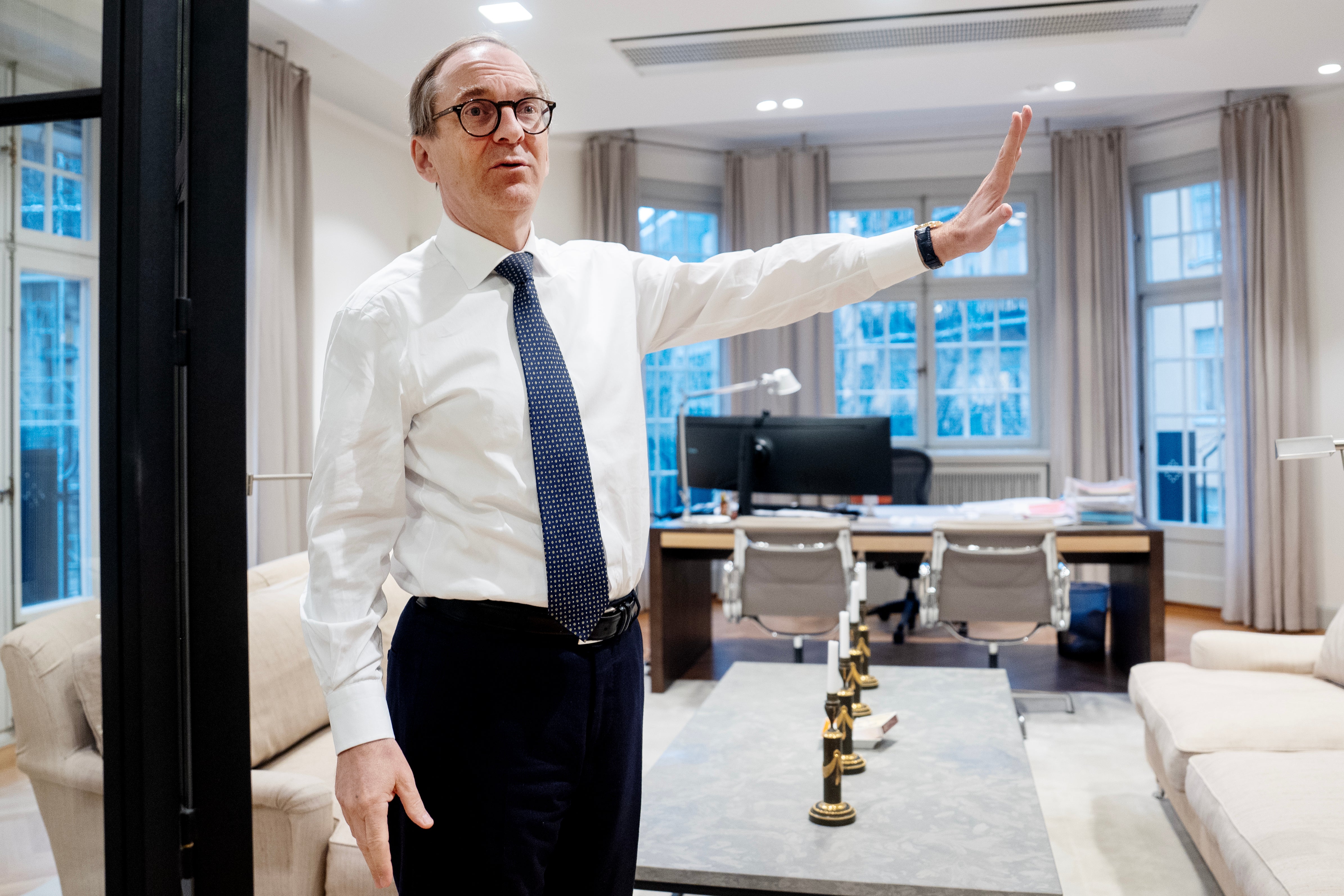 Porträttfoto av en man i vit skjorta och mörkblå slips som står i ett modernt kontorsrum med stora fönster.