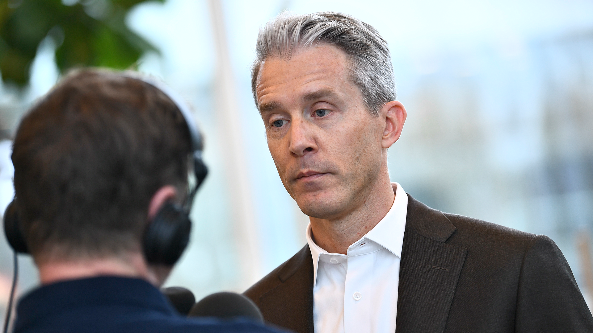 En man i kostym intervjuas av en journalist med mikrofon och hörlurar.