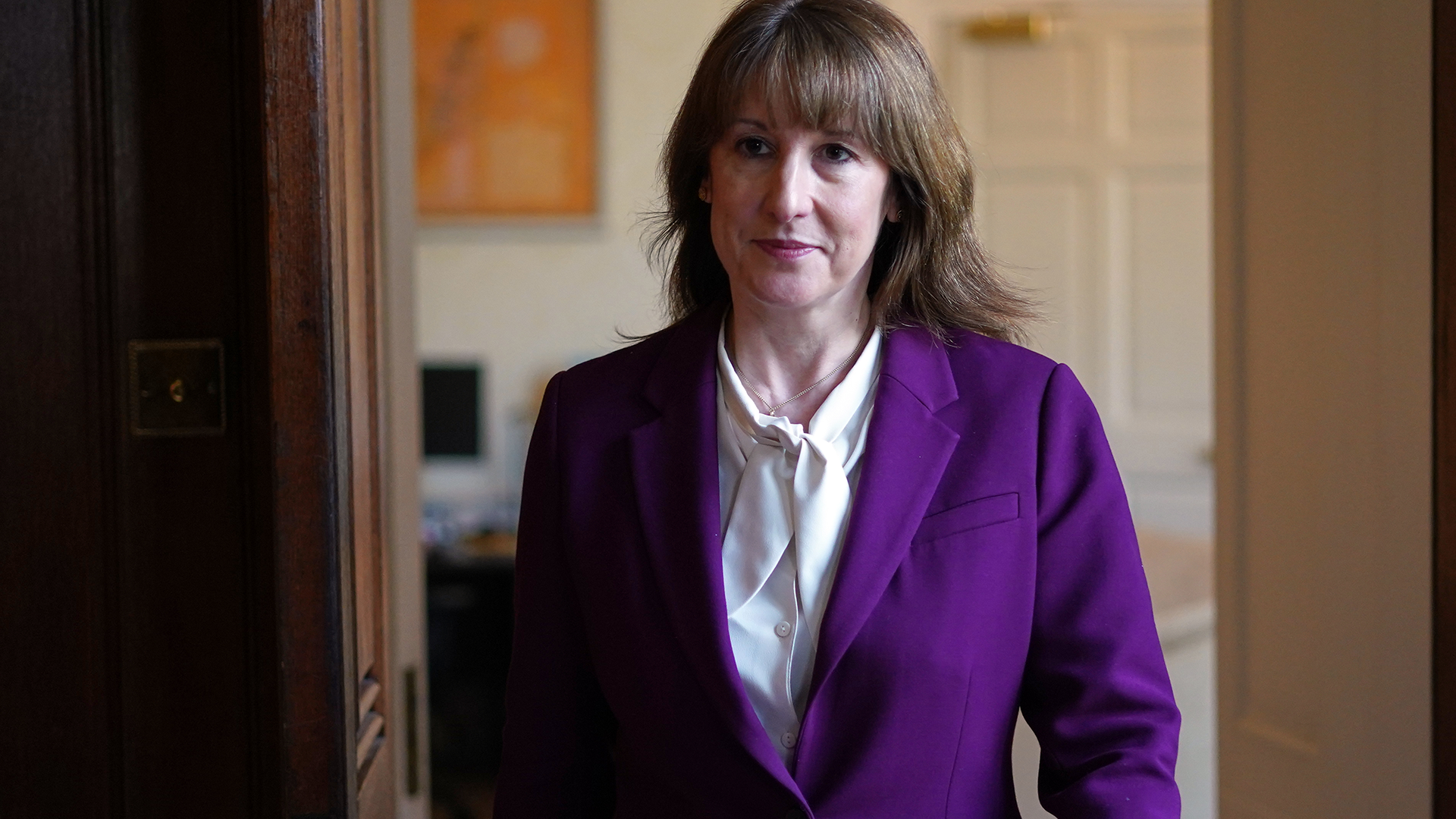 Porträttfoto av en kvinna i lila blazer och vit skjorta som står inomhus.