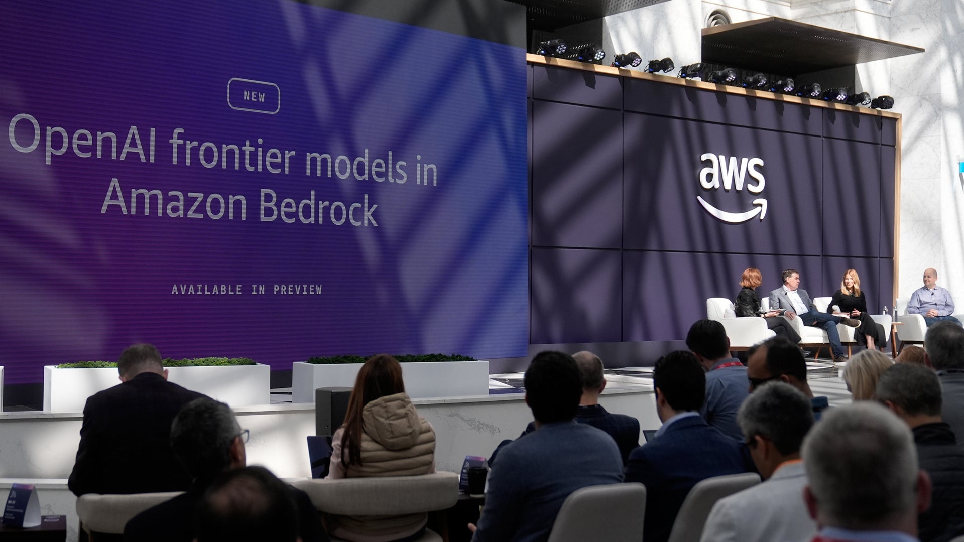 Publik tittar på ett samtal på en scen under en konferens. På en stor skärm står det "OpenAI frontier models in Amazon Bedrock" och på en vägg syns AWS-logotypen.