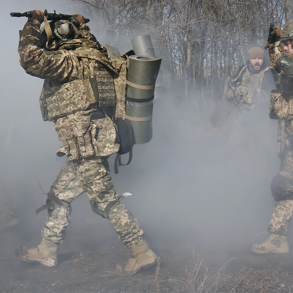 Tre soldater i kamouflageuniformer bär militär utrustning genom rök och damm.