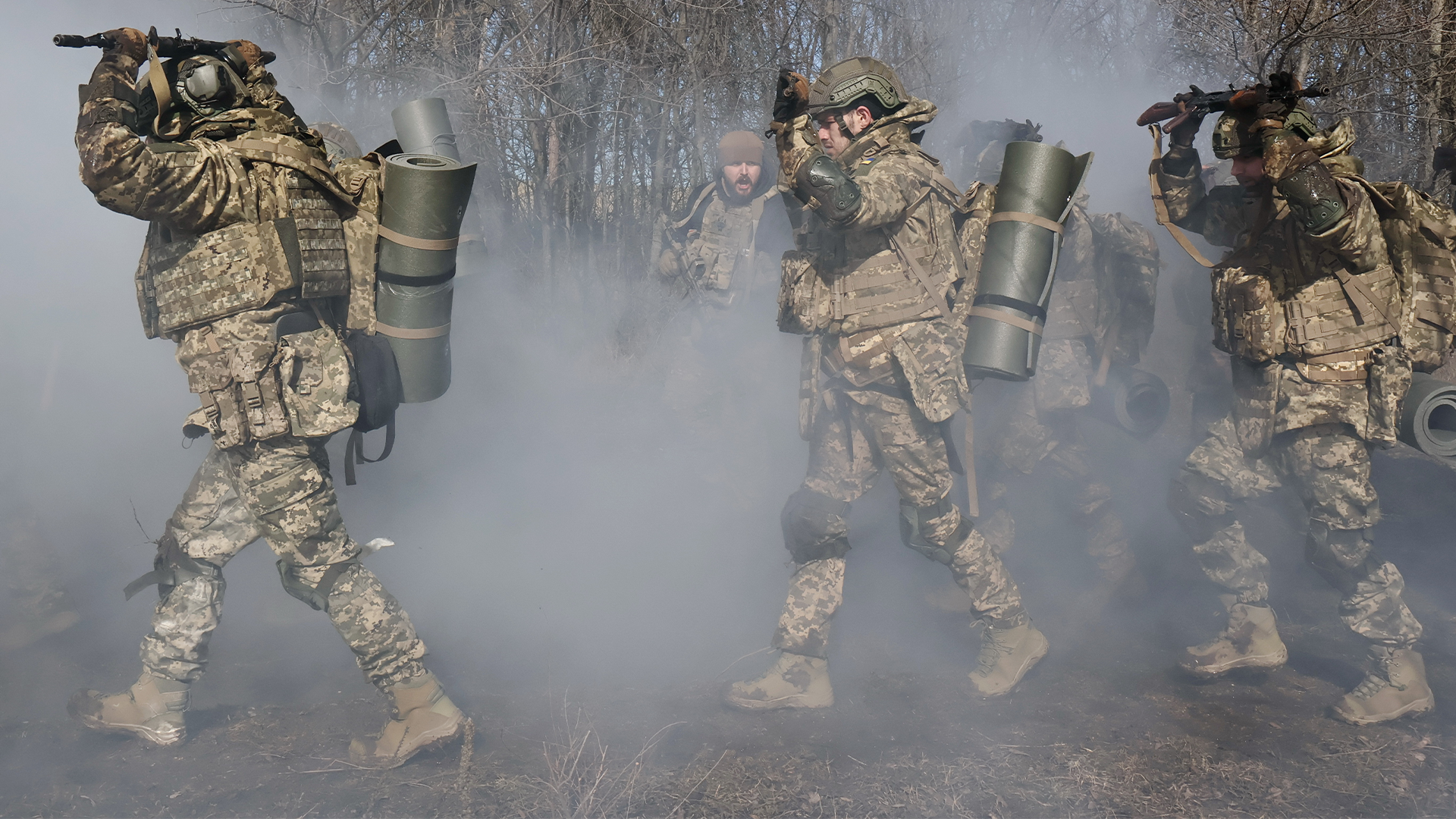 Tre soldater i kamouflageuniformer bär militär utrustning genom rök och damm.