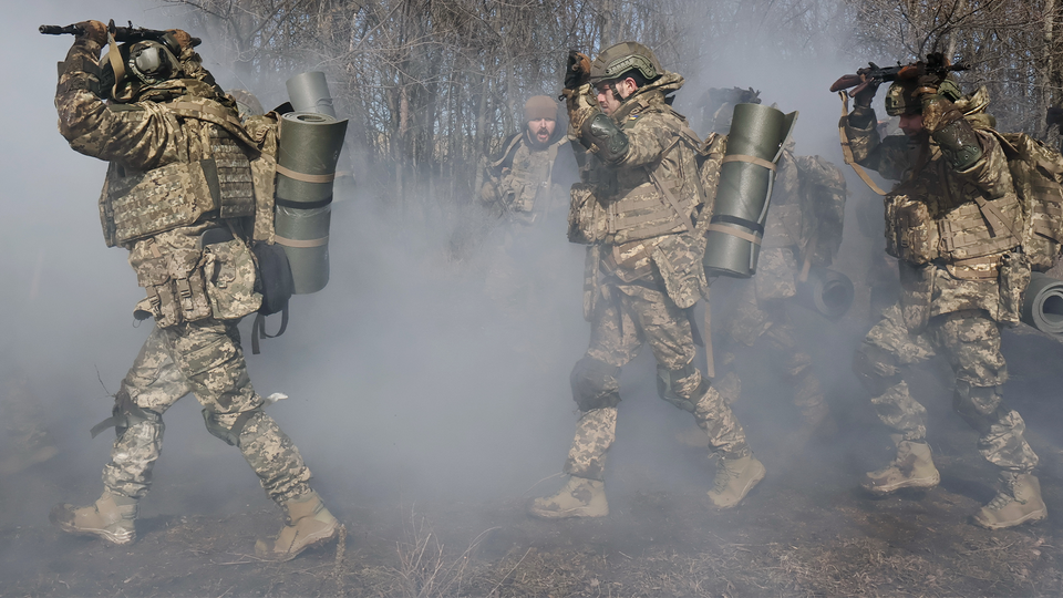 Tre soldater i kamouflageuniformer bär militär utrustning genom rök och damm.