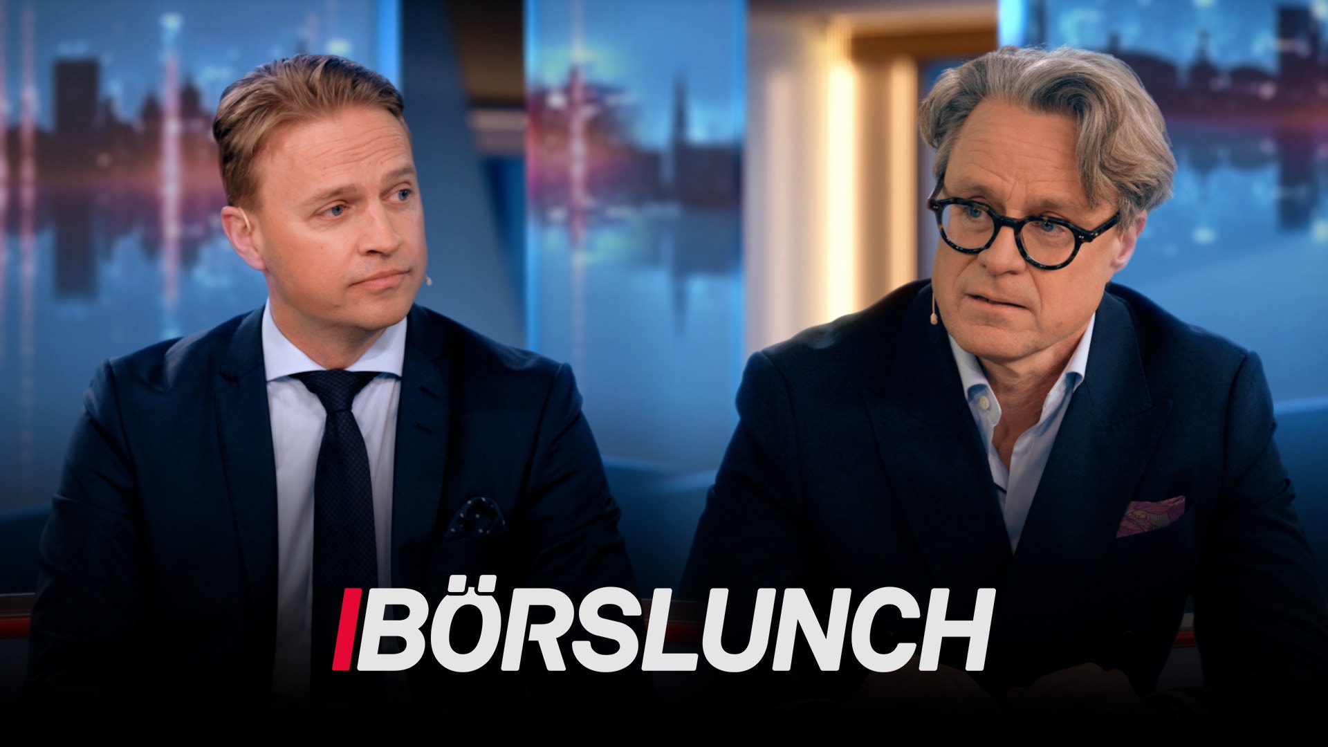 Två män i affärskläder sitter i en TV-studio med stadsvy i bakgrunden. Texten "BÖRSLUNCH" visas längst ned på skärmen.