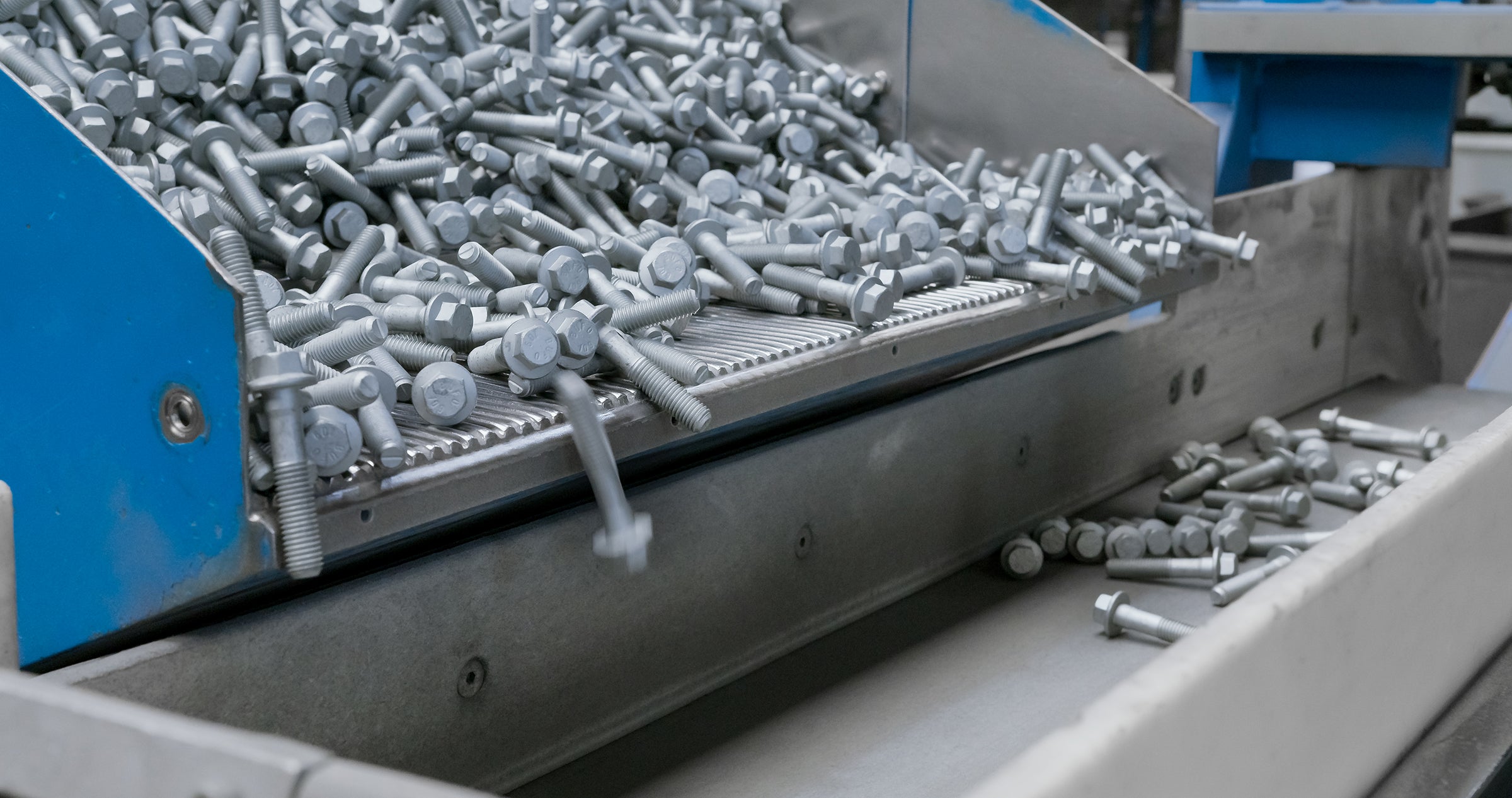 Industriell sorteringsmaskin som hanterar små metallskruvar. Maskinen har blå och grå komponenter, och skruvarna transporteras på en sorteringsyta där de organiseras och förpackas.
