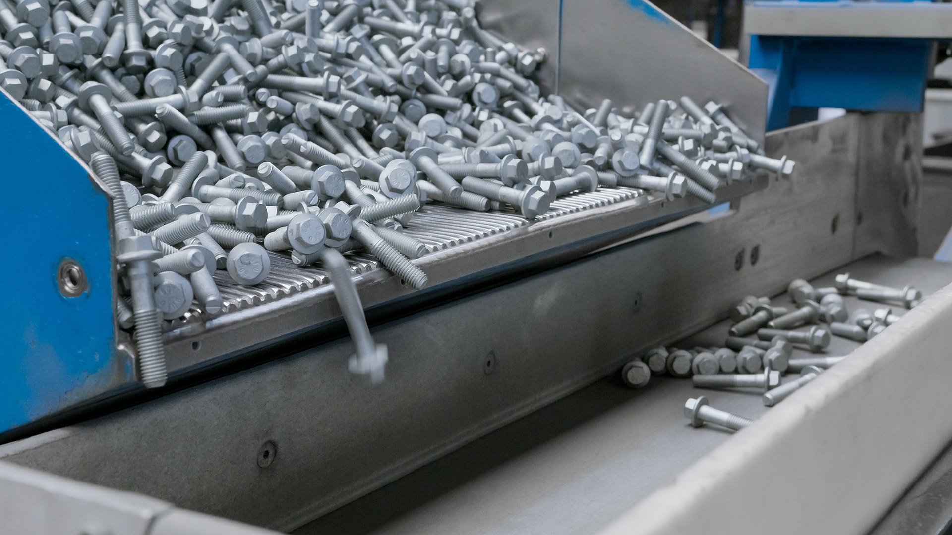 Industriell sorteringsmaskin som hanterar små metallskruvar. Maskinen har blå och grå komponenter, och skruvarna transporteras på en sorteringsyta där de organiseras och förpackas.