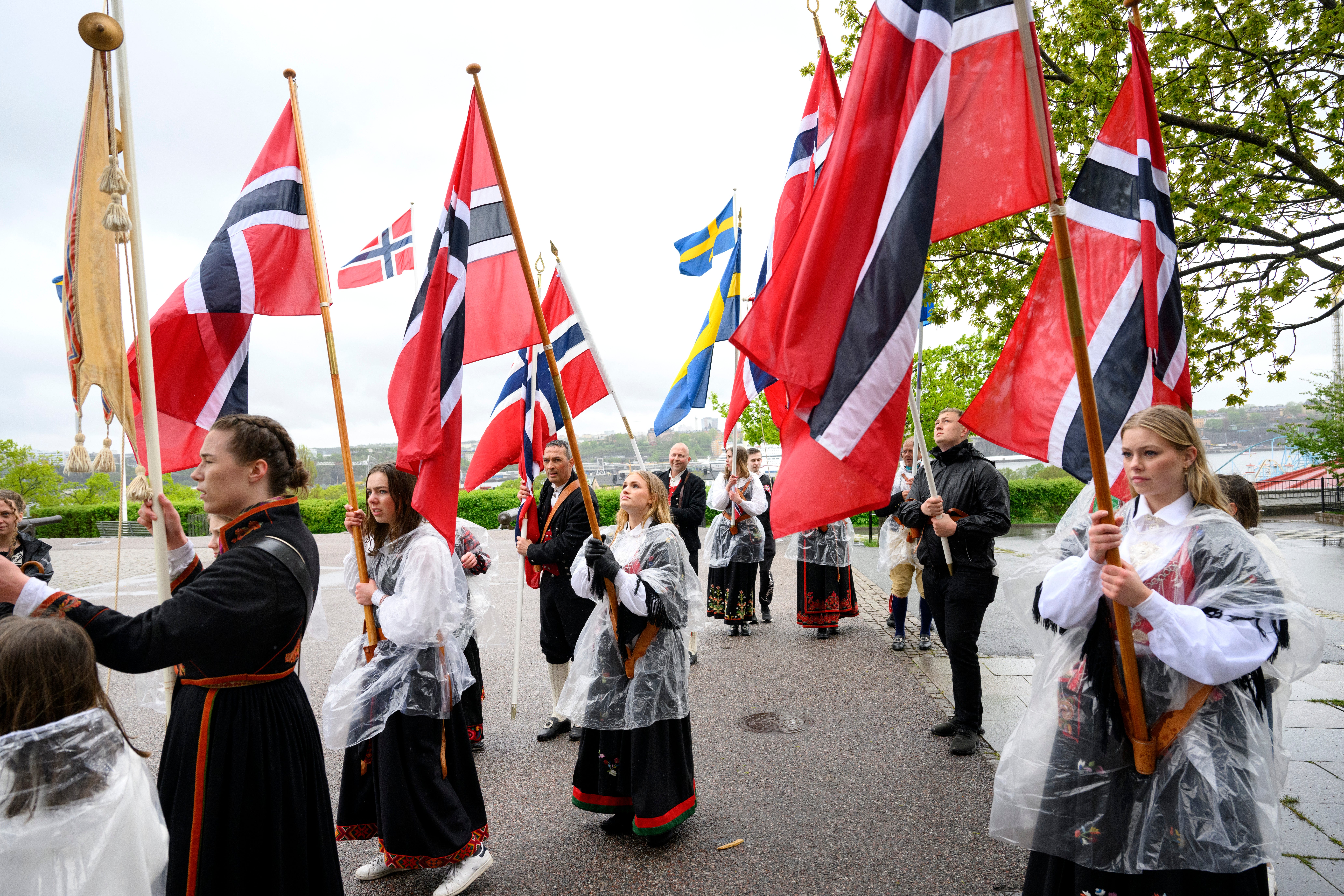 Grupp människor i traditionell nordisk dräkt håller norska flaggor under en kulturell fest eller parade.
