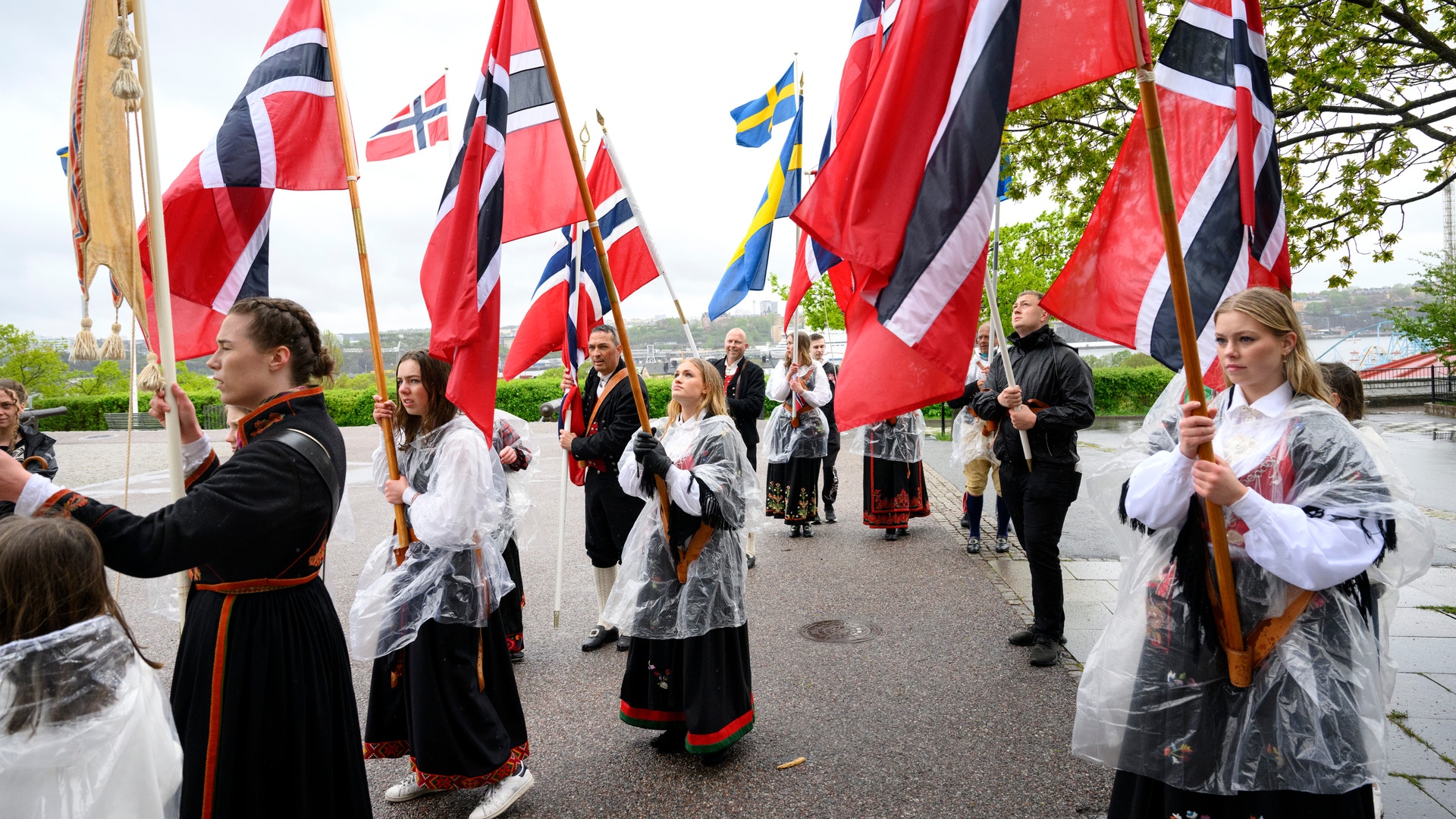 Grupp människor i traditionell nordisk dräkt håller norska flaggor under en kulturell fest eller parade.