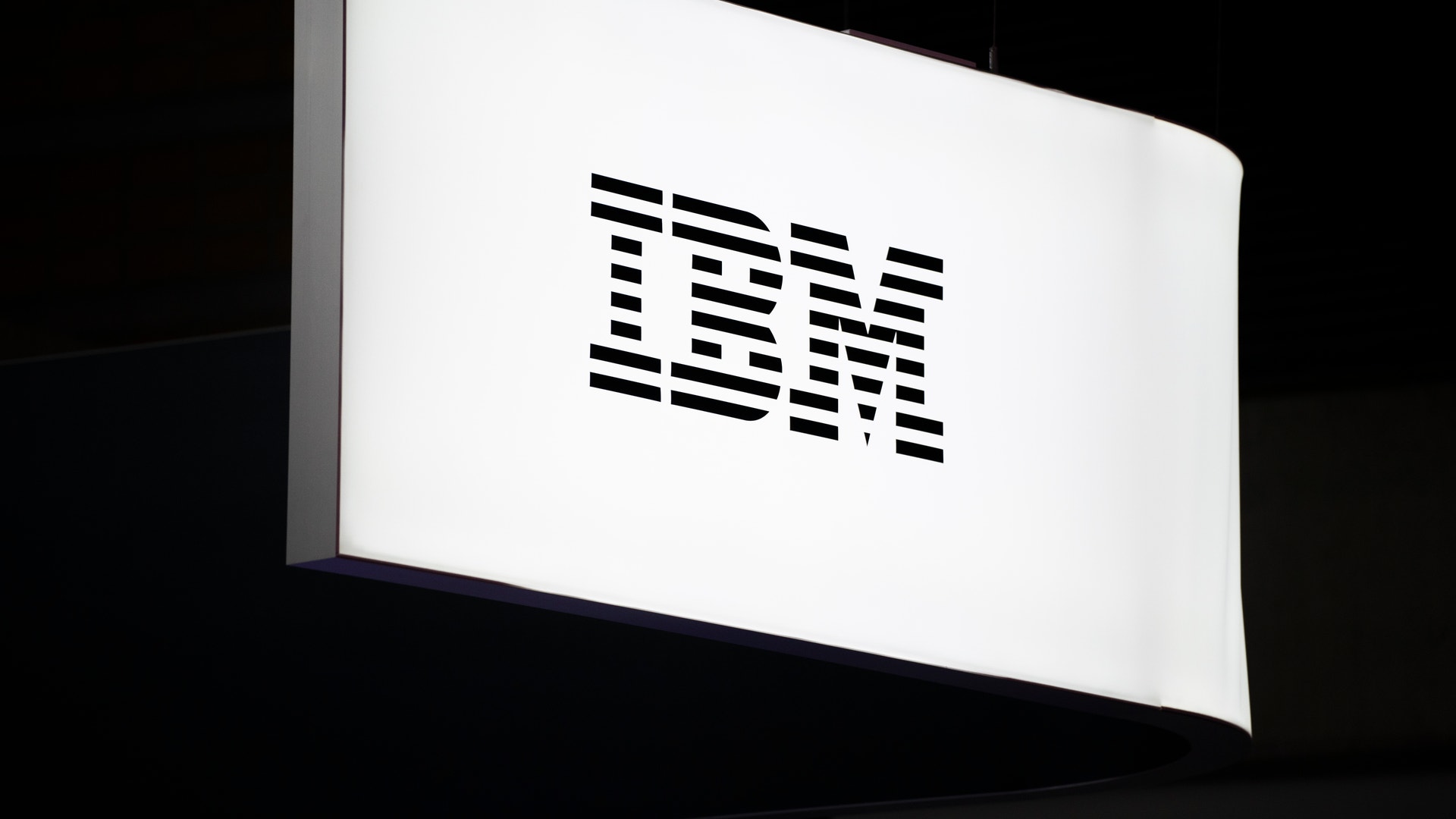En vit belyst skylt med IBM-logotypen mot mörk bakgrund.