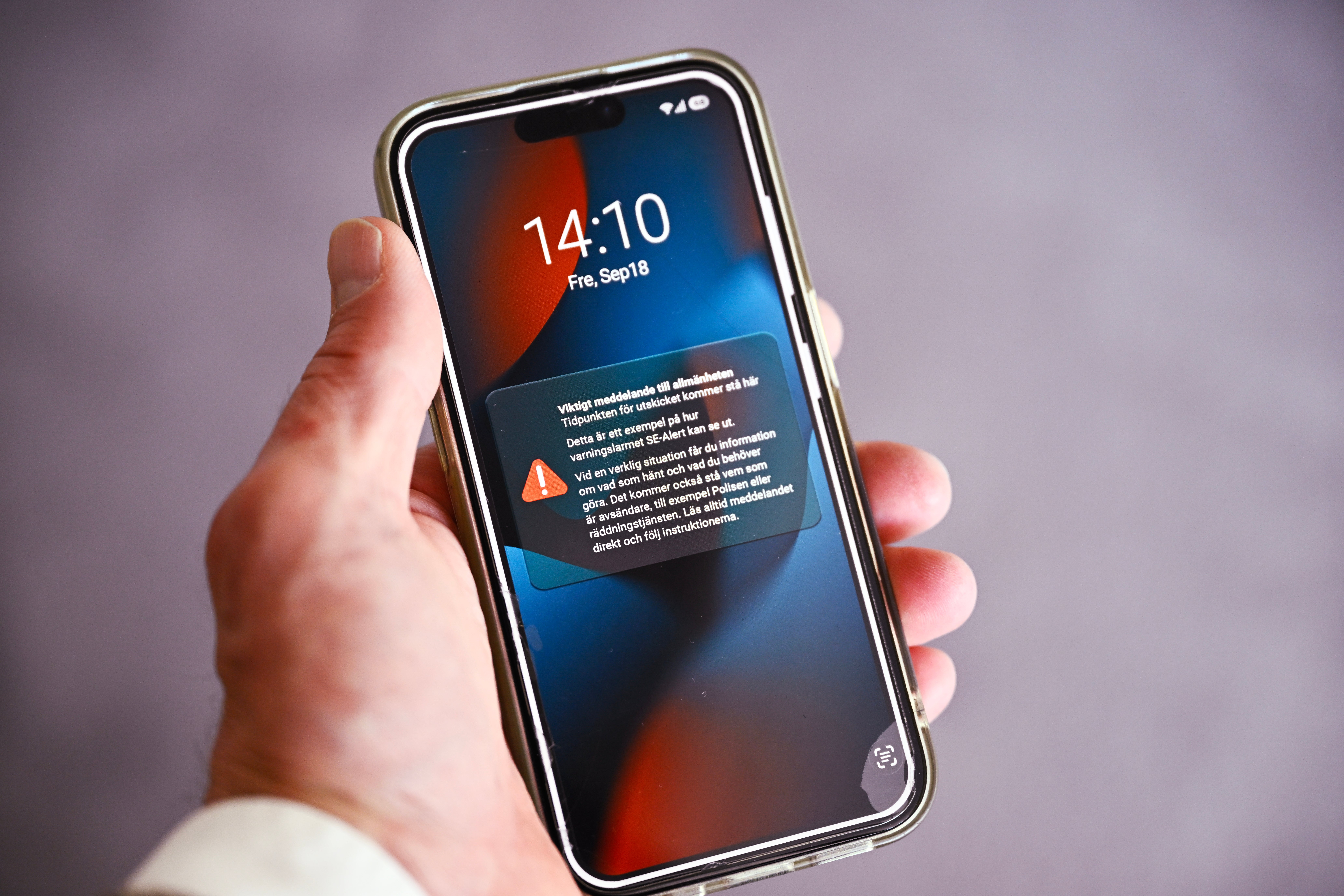 En hand håller en smartphone som visar en varningsmeddelande på skärmen.