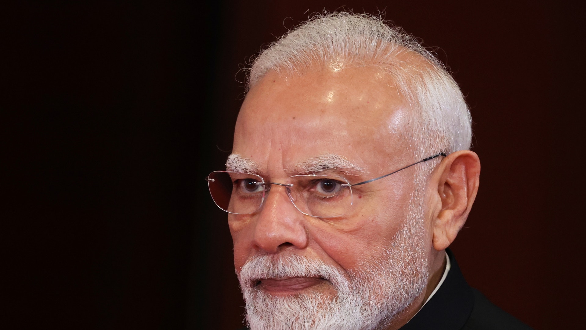 Närbild av Narendra Modi, en äldre man med vitt hår och skägg, glasögon och mörk jacka.