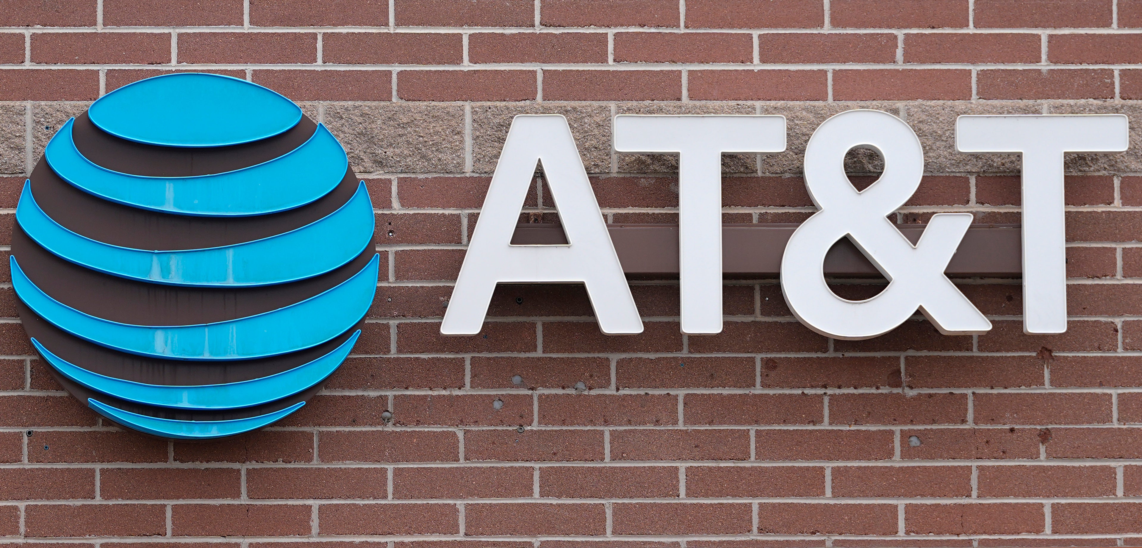 AT&T:s logotyp monterad på en tegelvägg. Logotypen visar en blå glober med horisontella streck och vita bokstäver.