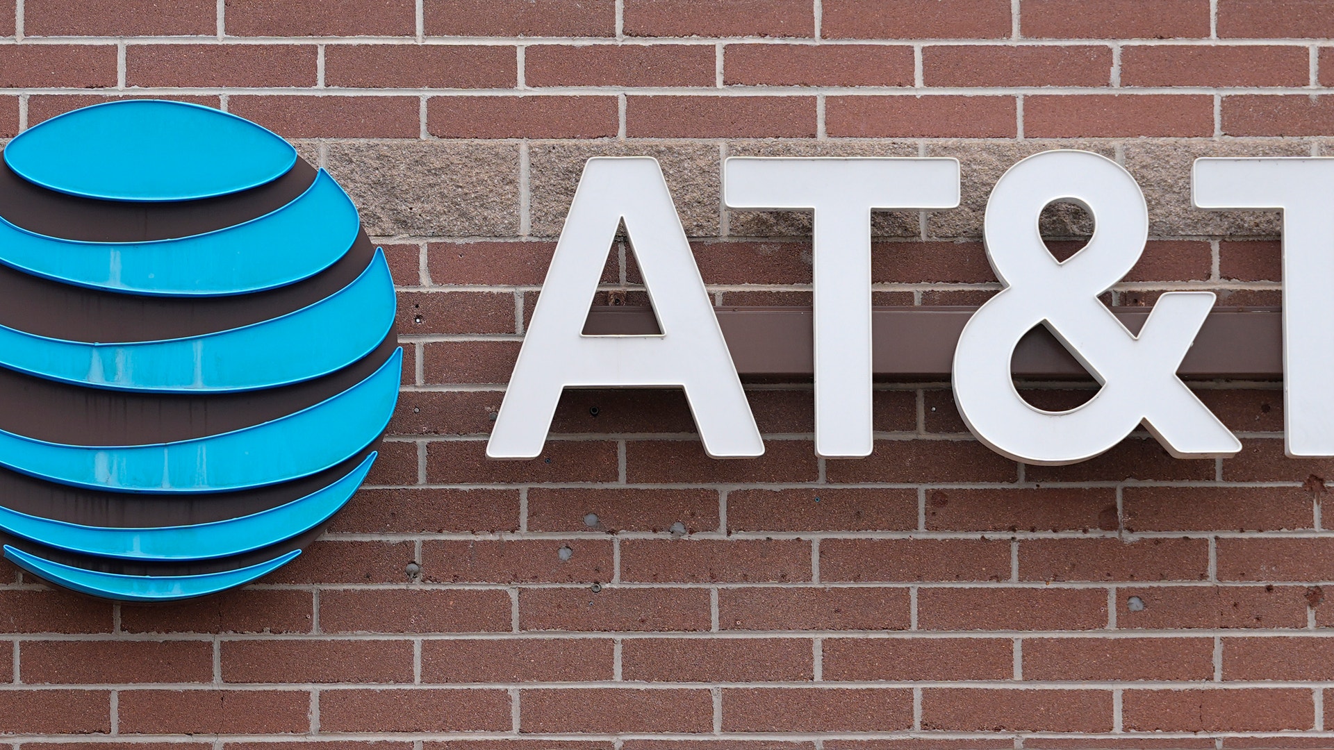 AT&T:s logotyp monterad på en tegelvägg. Logotypen visar en blå glober med horisontella streck och vita bokstäver.