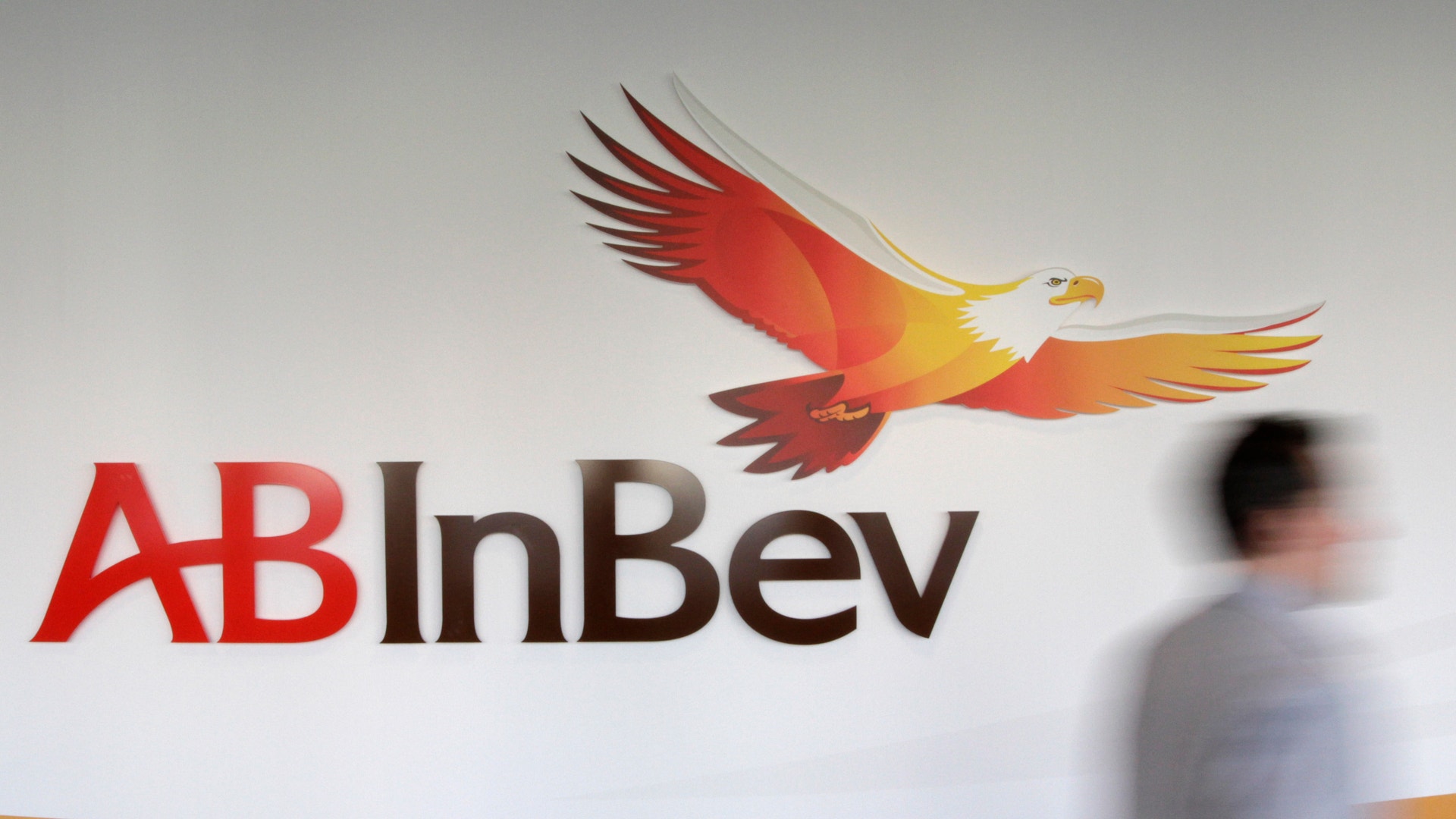 AB InBev-logotyp med en röd och gul örn på en vägg. En person går förbi i bakgrunden.