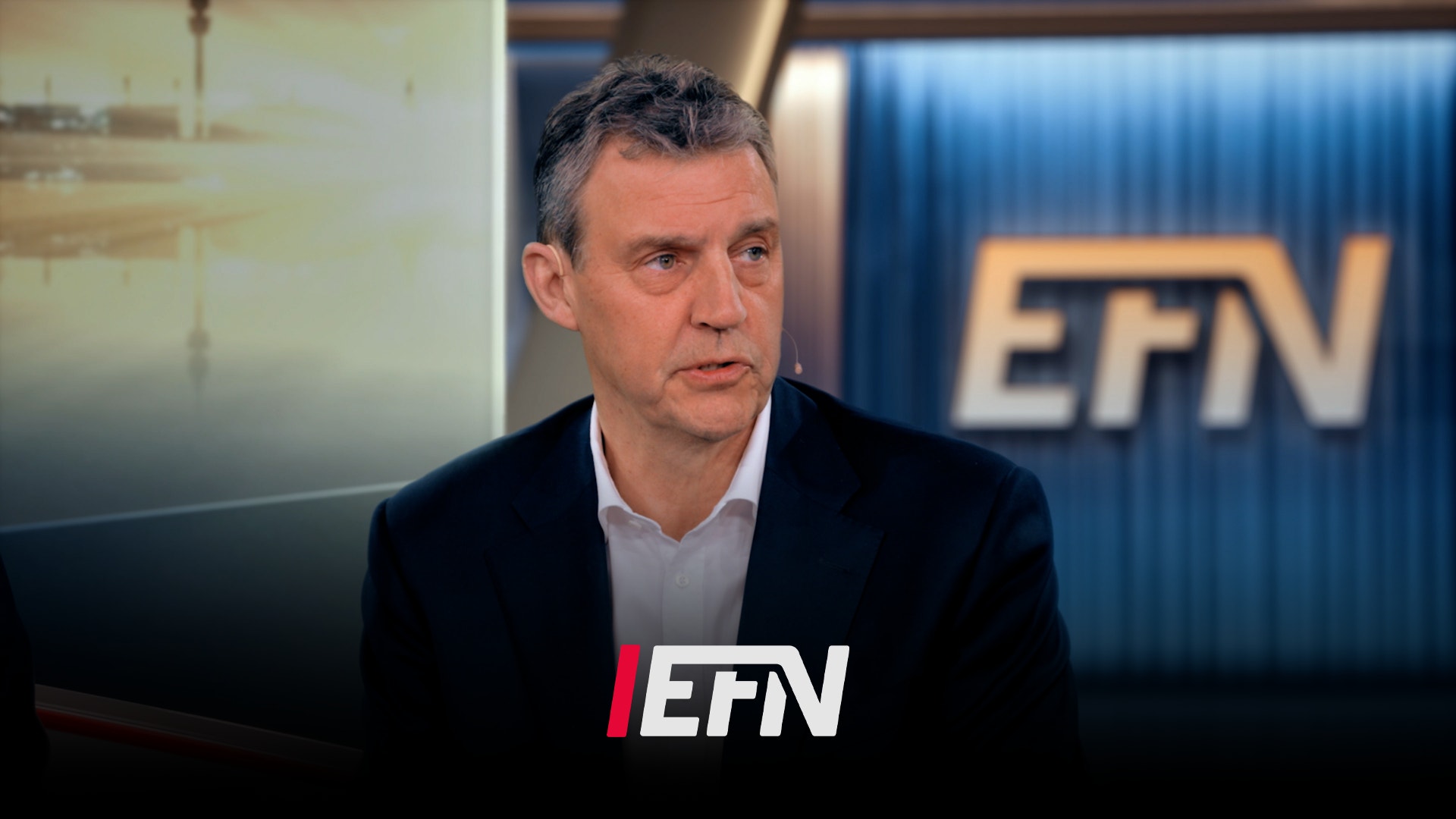 Man i kostym under intervju i TV-studio med EFN-logotyp i bakgrunden.