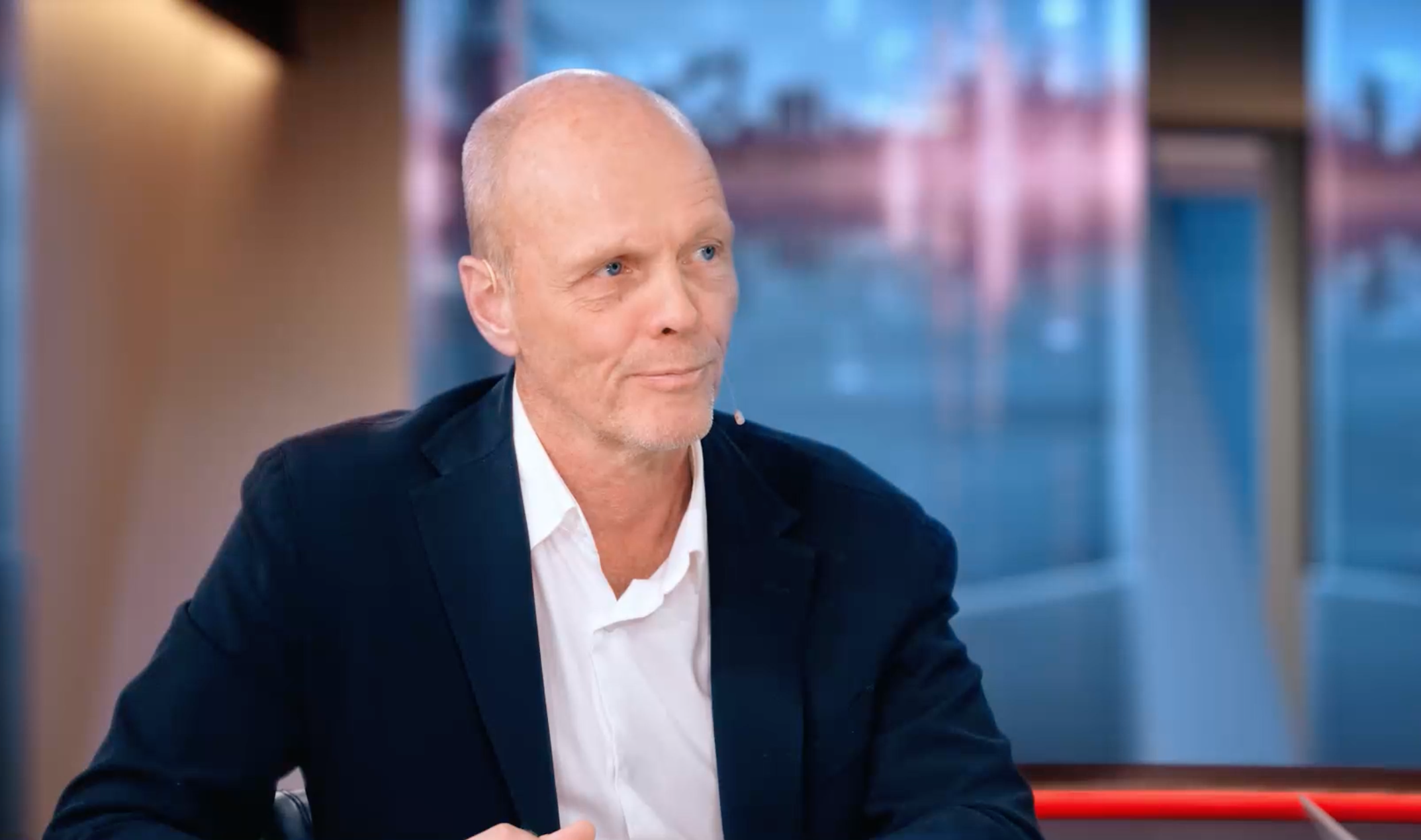 Man i kavaj sitter i en tv-studio under en intervju.