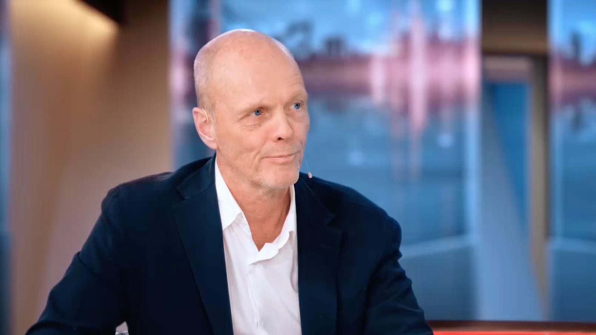 Man i kavaj sitter i en tv-studio under en intervju.