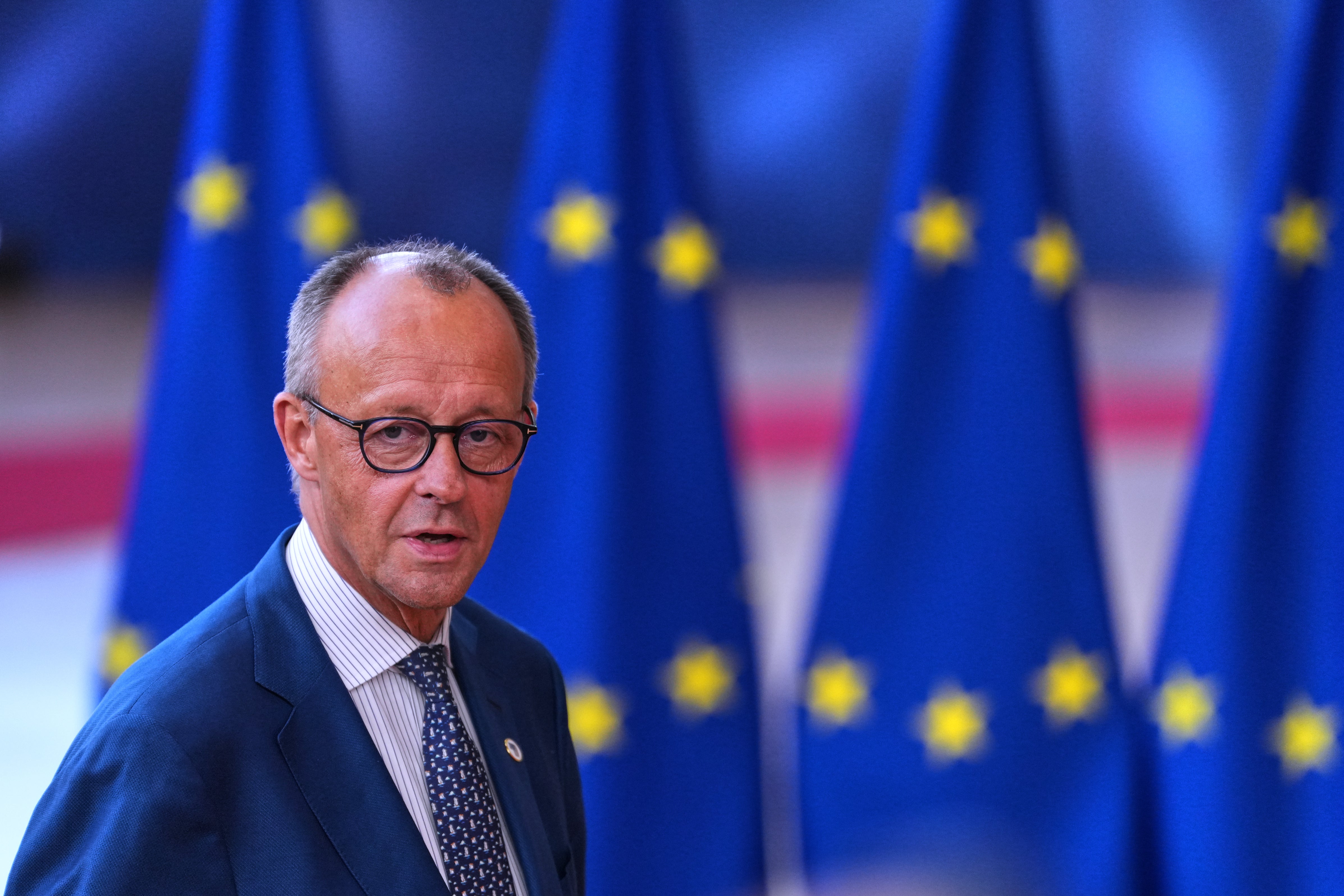 Man i kostym och glasögon framför EU-flaggor