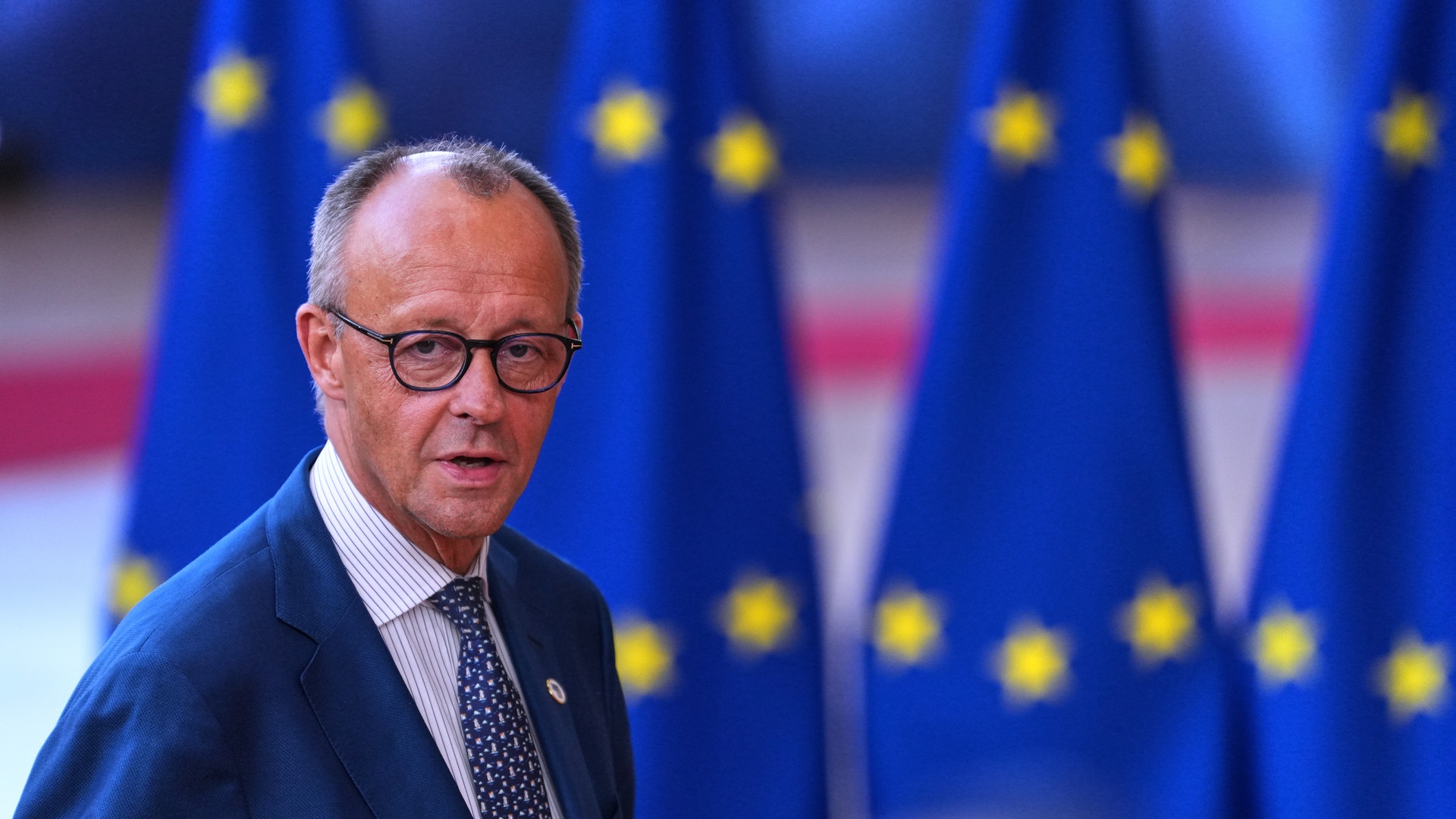 Man i kostym och glasögon framför EU-flaggor