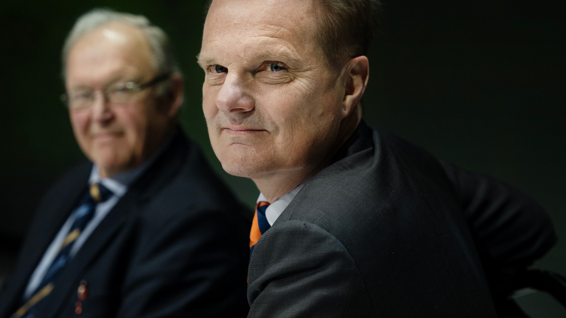 Två affärsmän i kostym fotograferade mot mörk bakgrund