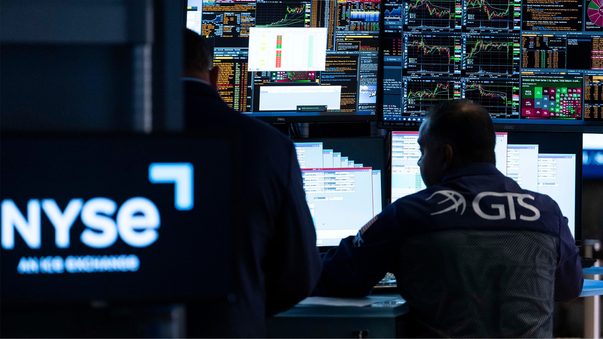 En person arbetar vid flera datorskärmar på New York Stock Exchange. Skärmarna visar finansiella grafer och marknadsdata i olika färger.
