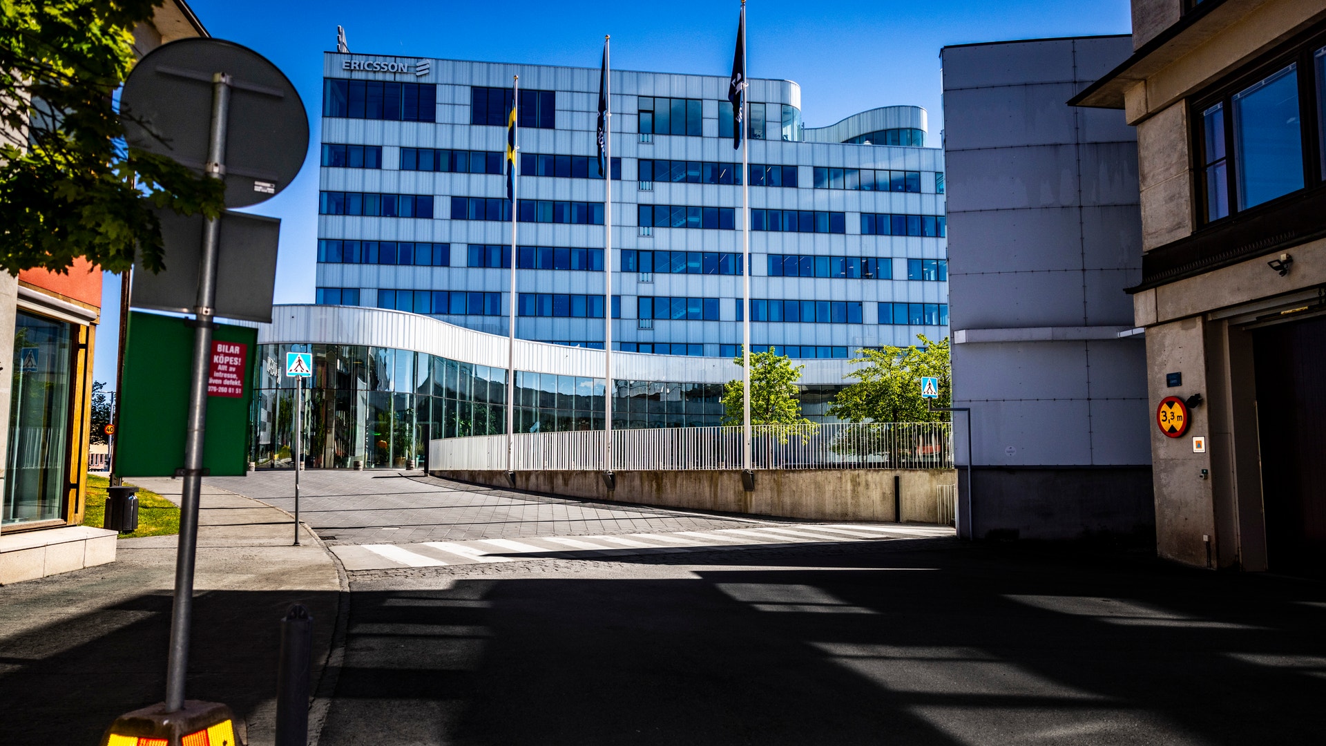 En modern blå kontorsbyggnad sett från en stadsgata med träd och andra byggnader omkring.