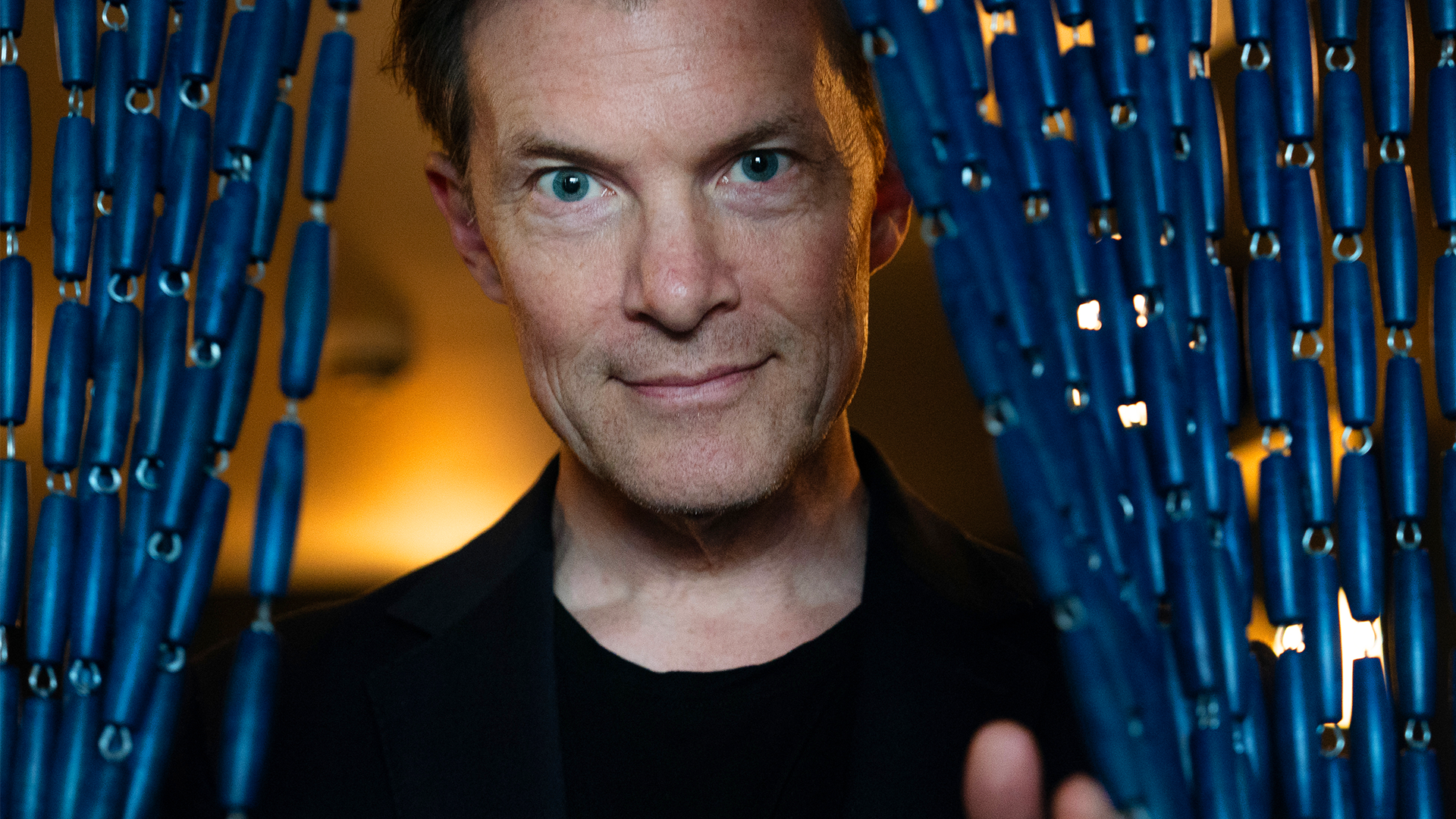 Författaren Johan Norberg som tittar ut genom en draperidörr.