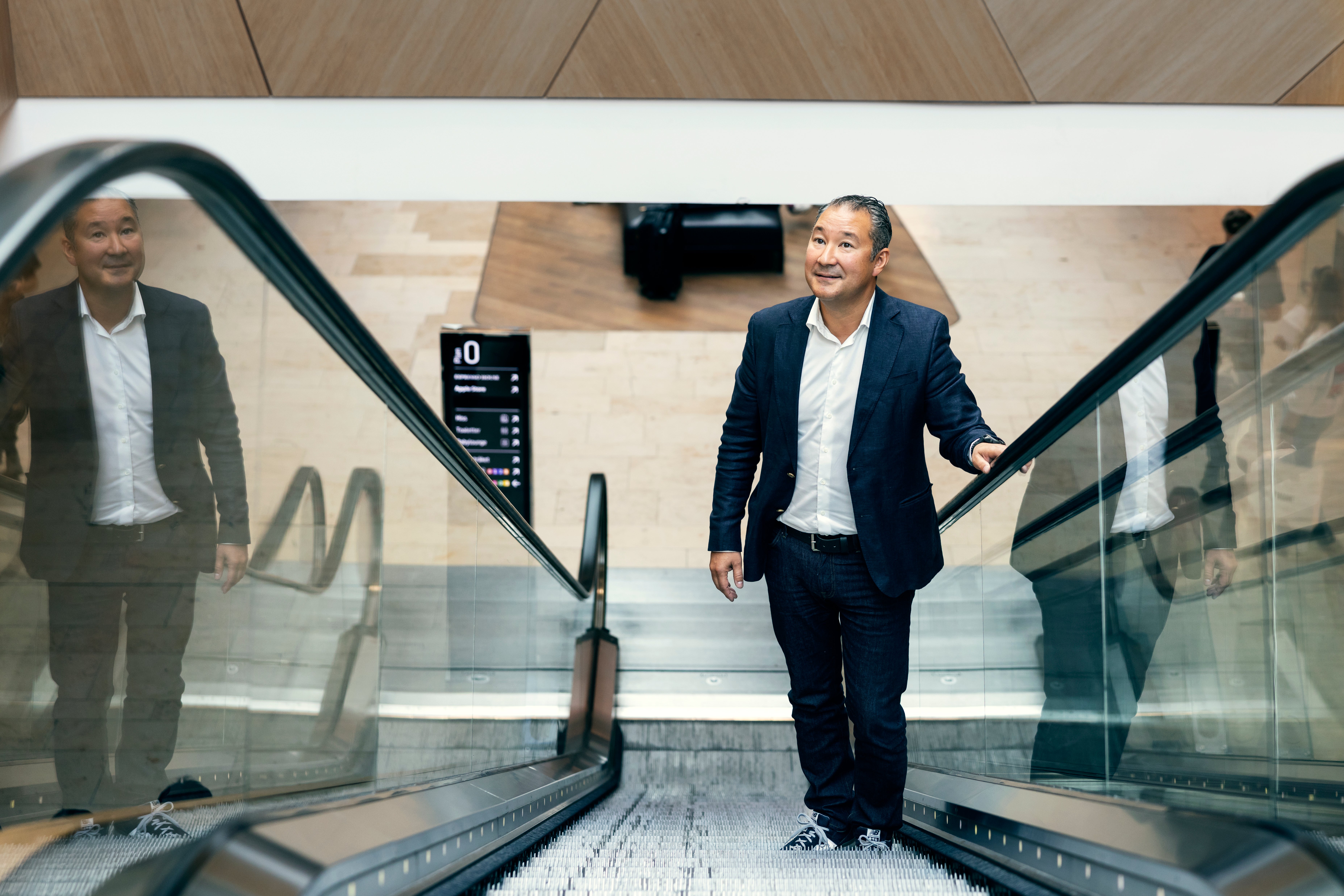 Två personer i affärskläder på en rulltrappa i en modern byggnad. Kvinnan till höger ser glad ut medan mannen till vänster står bakom henne.