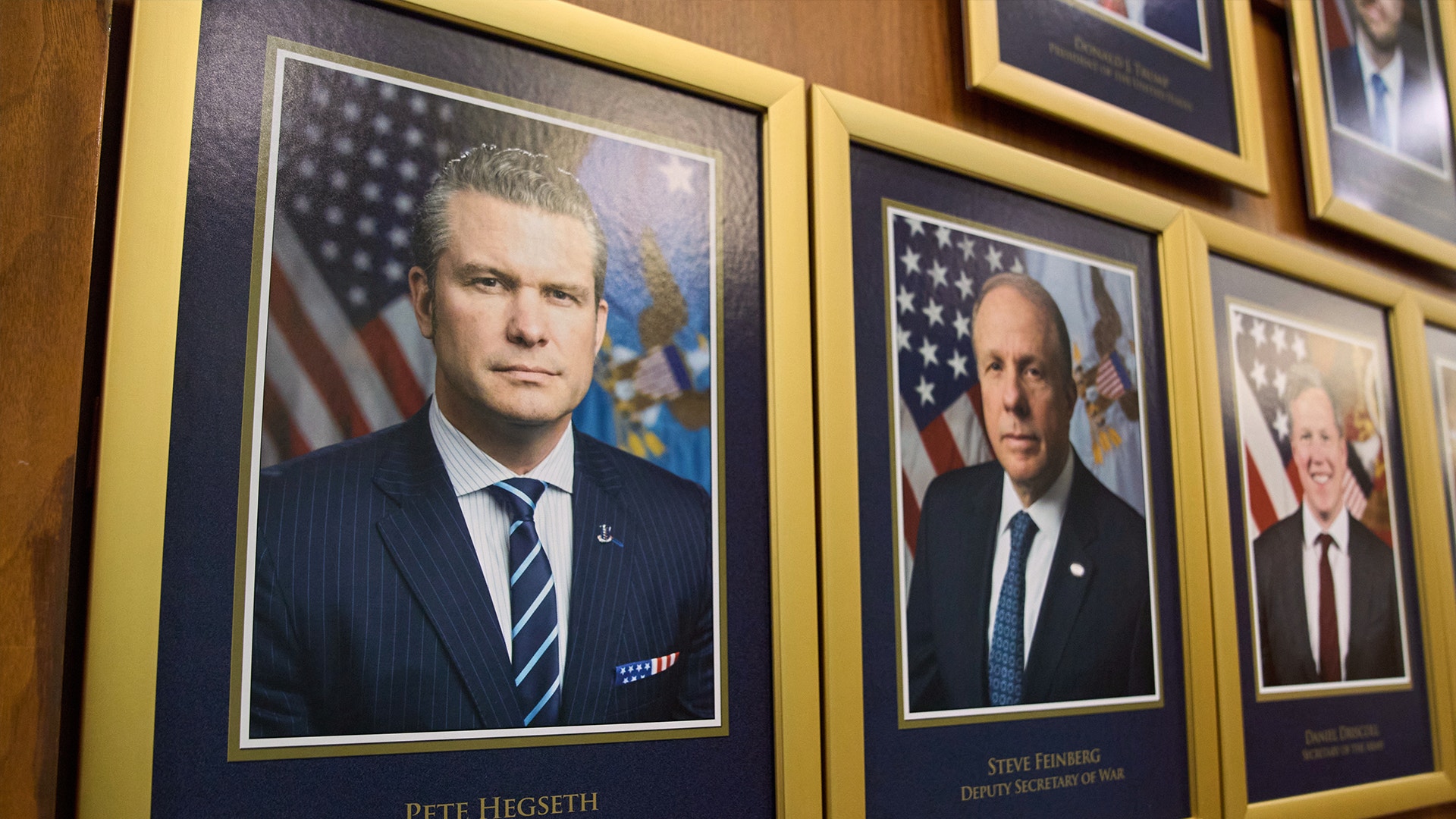 Inramade porträtt av män i formella kläder hängande på vägg med amerikanska flaggor i bakgrunden.