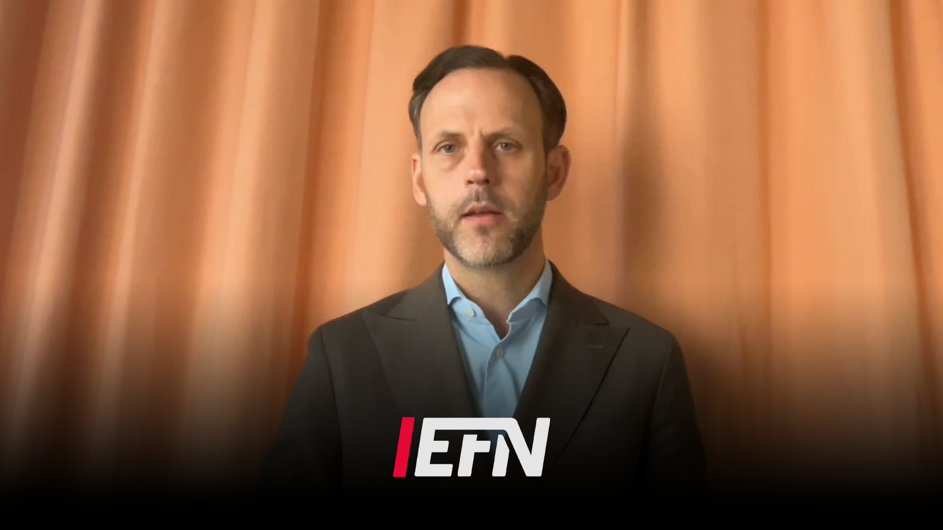 Porträtt av en man i svart kavaj och ljusblå skjorta framför en orange bakgrund med EFN-logotyp.