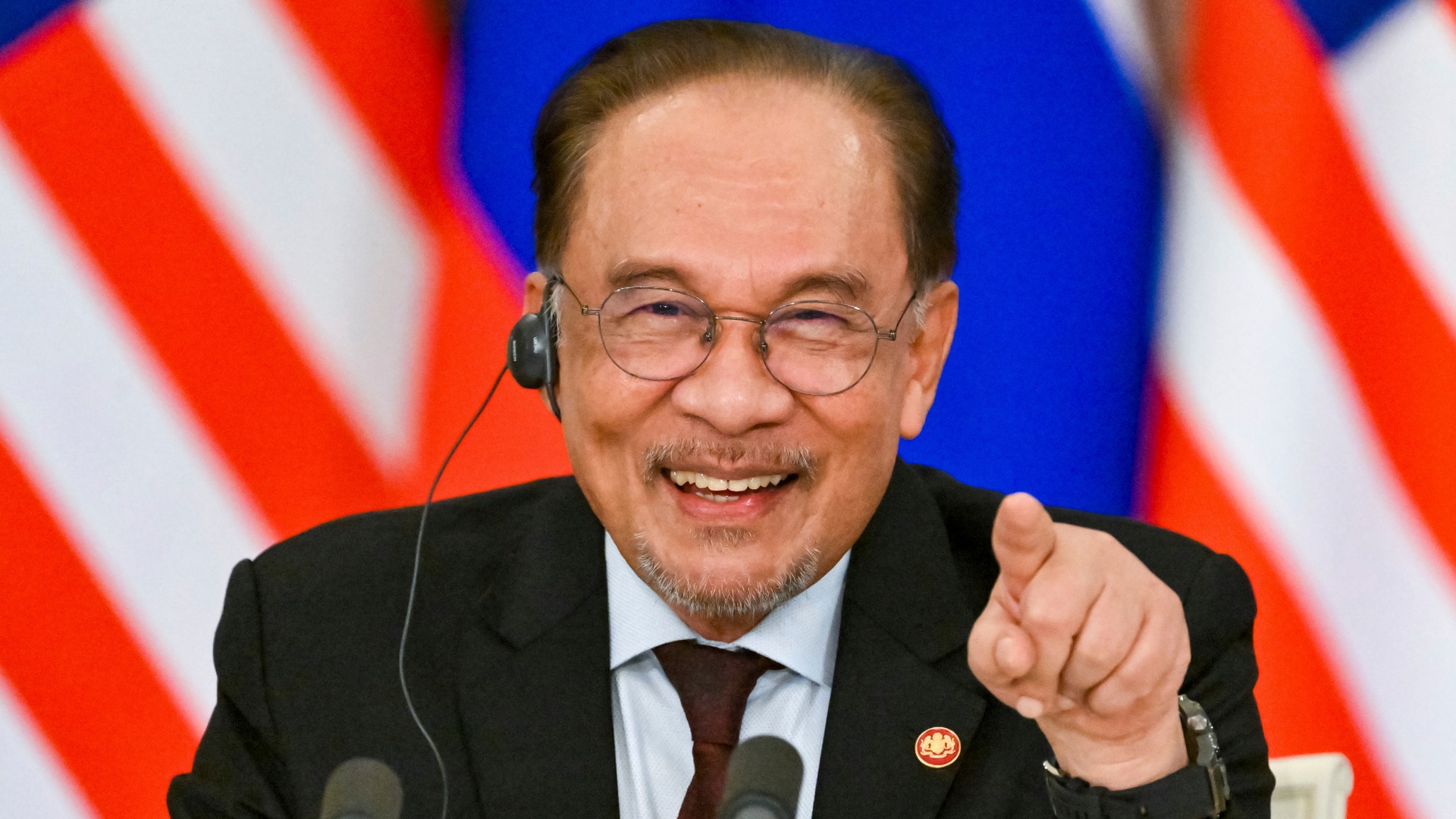 Anwar Ibrahim ler och pekar glatt in i kameran vid en presskonferens.