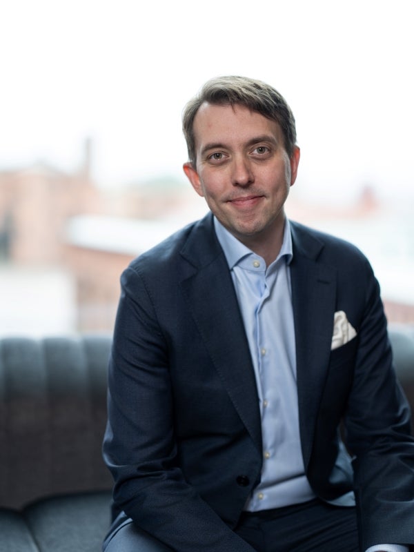 Porträtt av en man i kostym som sitter och ler mot kameran.