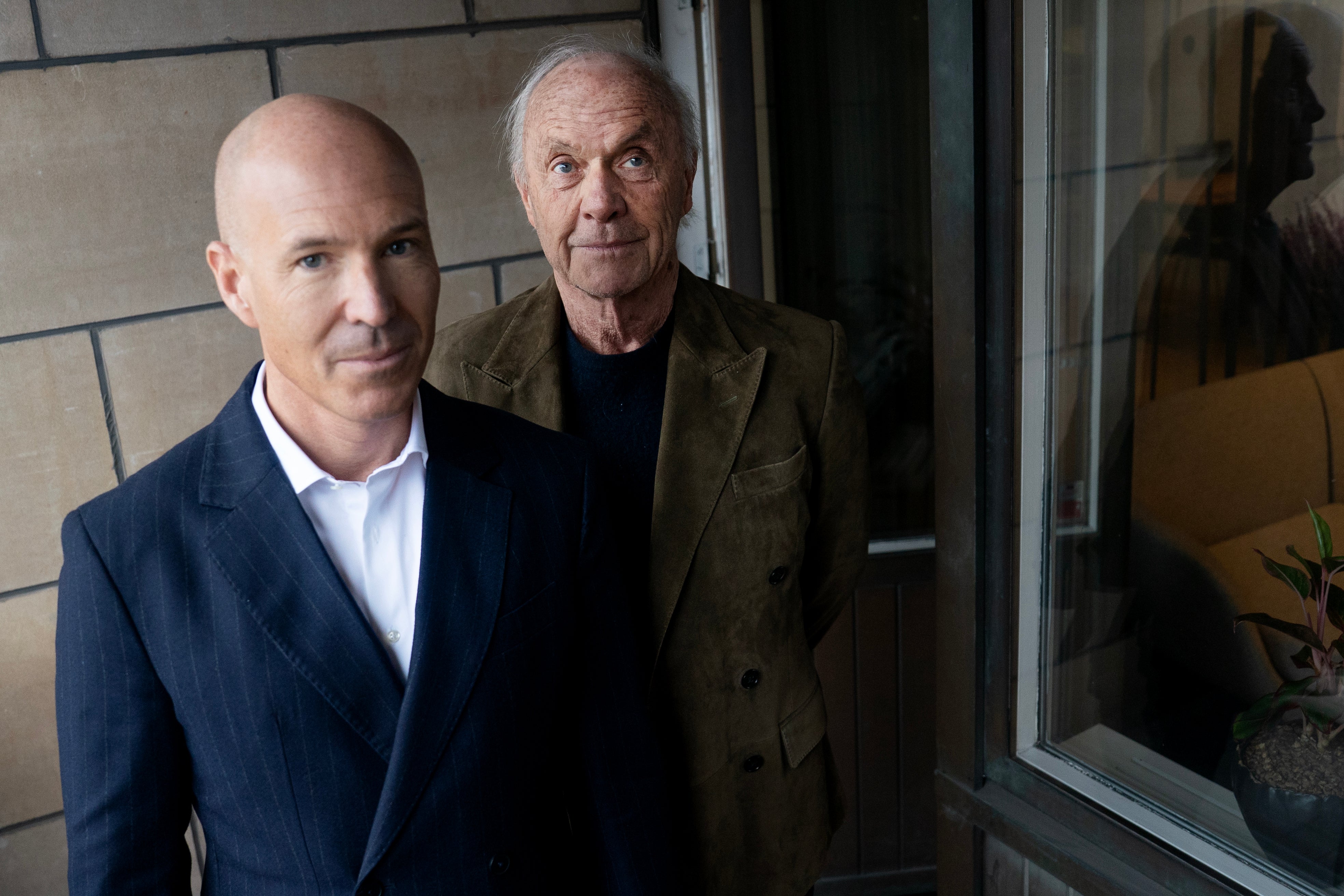 Två män står tillsammans framför en vägg med moderna kakel och ett fönster.