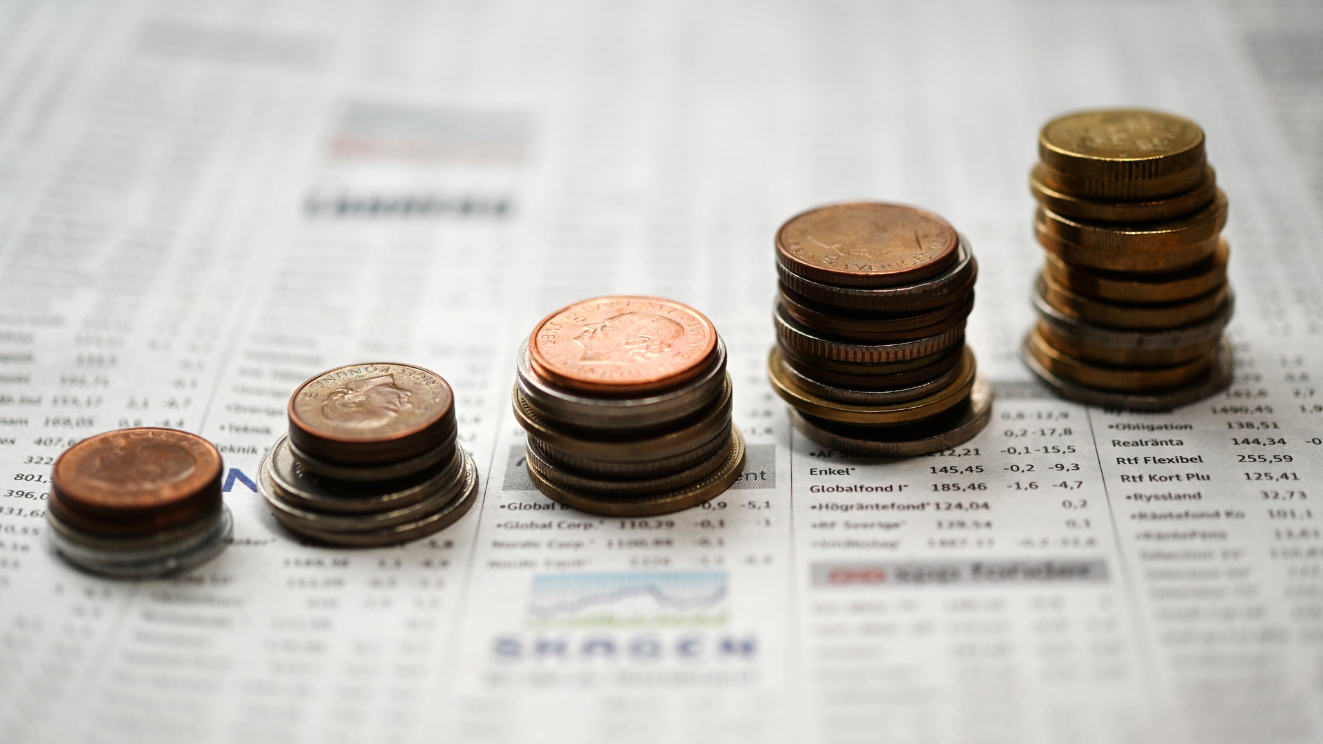 Staplar av mynt i ökande höjd på en finansiell tidning, som symboliserar ekonomisk tillväxt och investeringar.