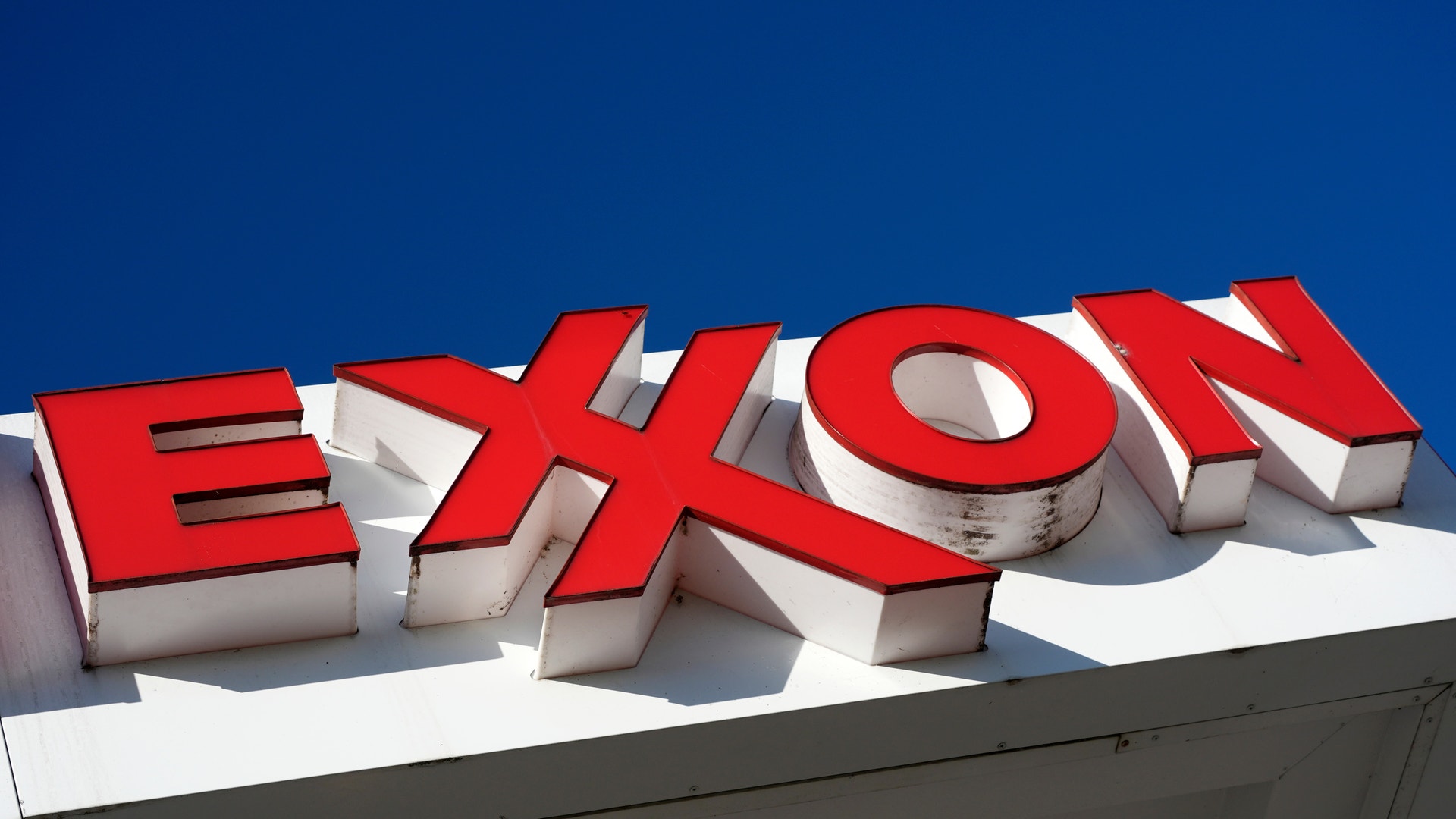 Rött och vitt 3D-skyltsignage med texten "EXON" på ett byggnadstaktak mot blå himmel.