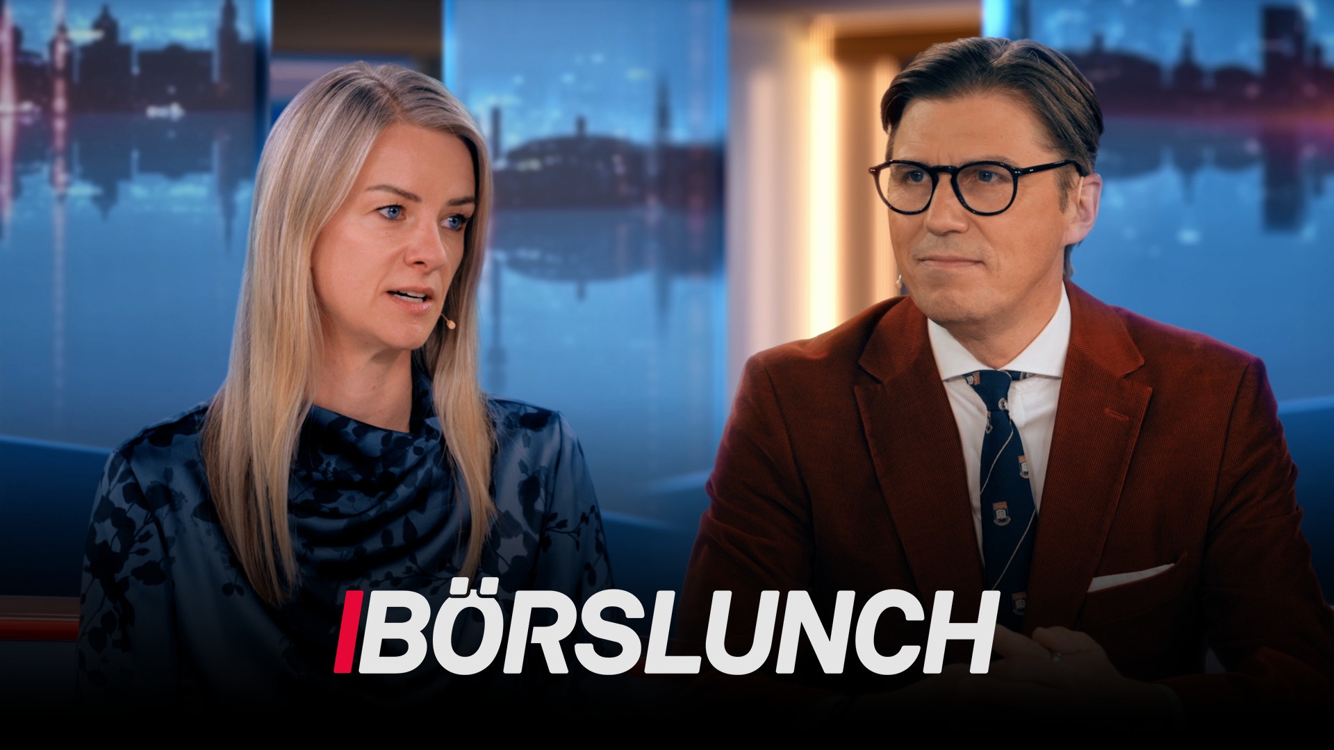 En man och en kvinna sitter vid ett studiobord under en TV-sändning kallad Börslunch. I bakgrunden syns en stadshorisont.