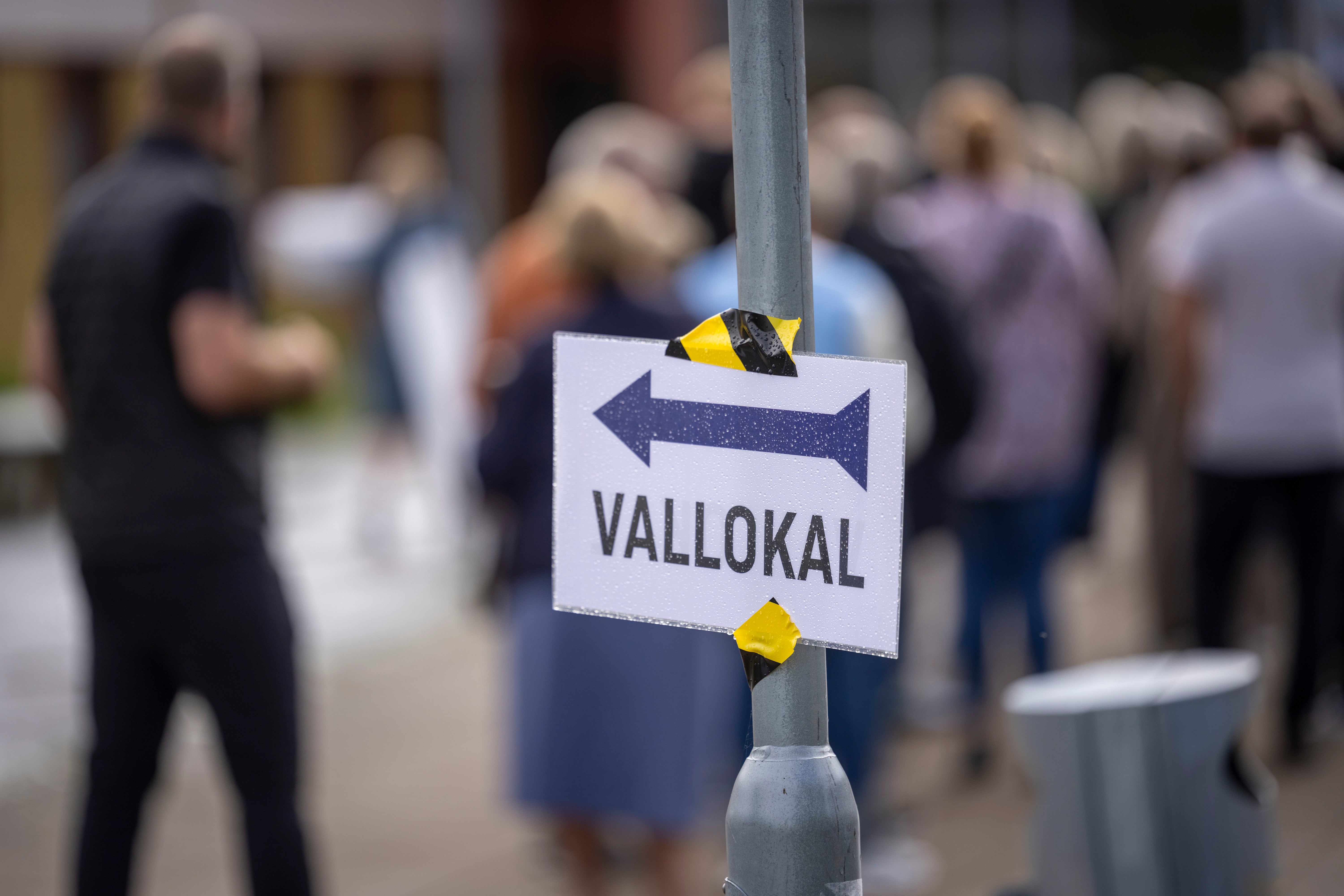 En skylt med texten "Vallokal" och en pil, med kö av människor i bakgrunden.