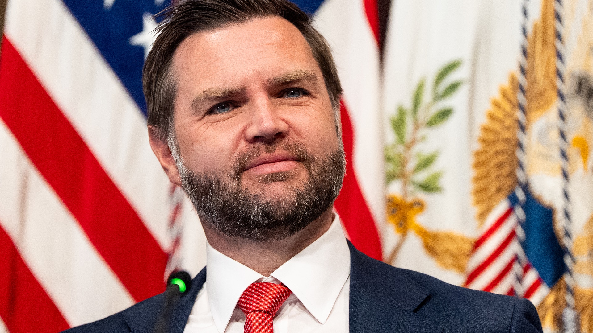 Man i mörk kostym och röd-vit randig slips framför amerikanska flaggor
