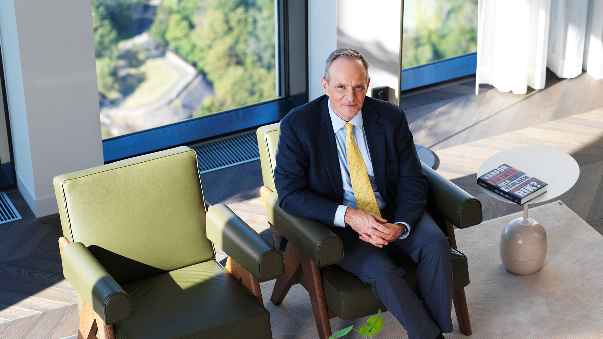 Simon Johnson sitter i en fåtölj i kostym i ett solig ljus våning.