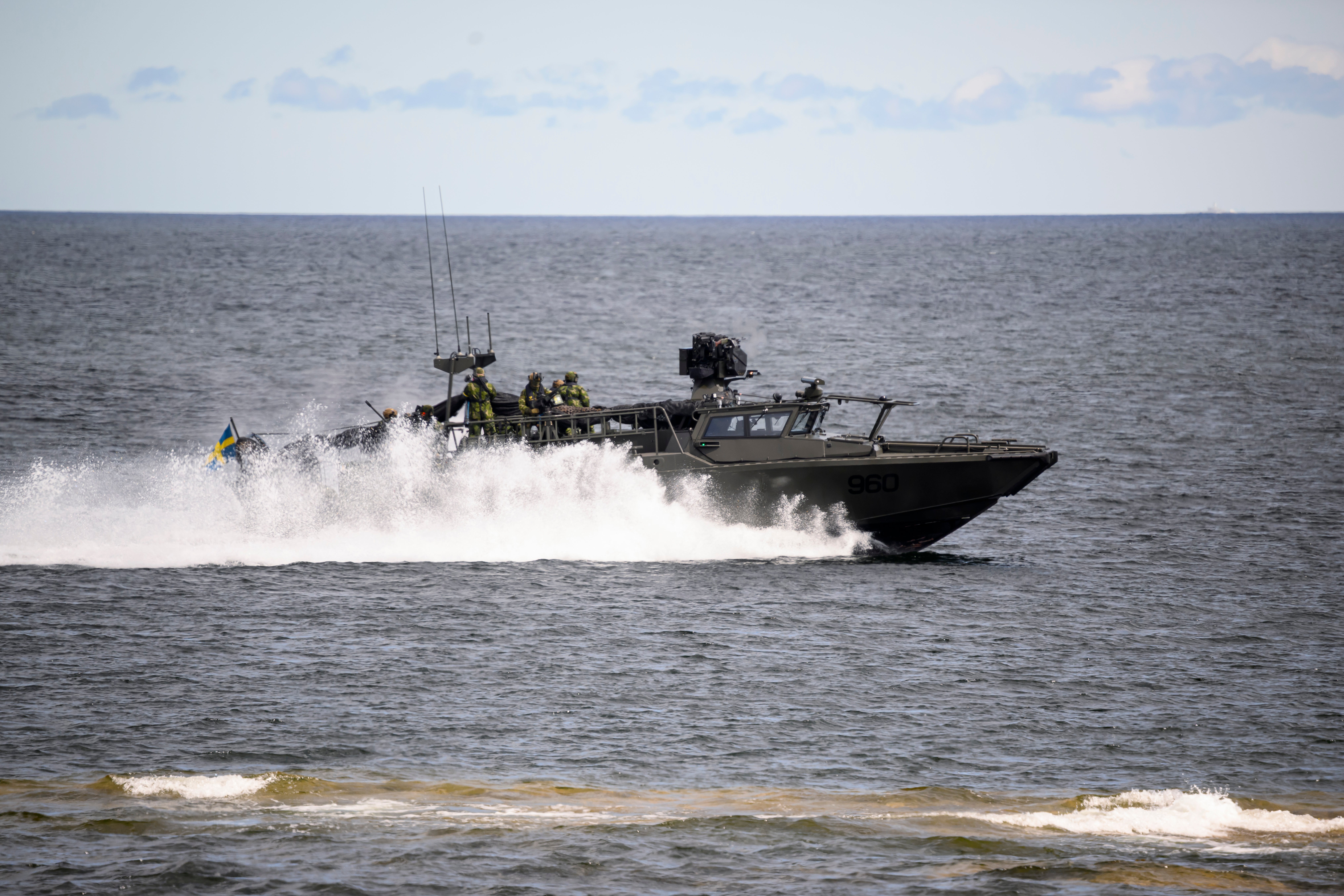En militär snabbgående båt med soldater ombord kör genom havet och skapar stora vattenstänk.