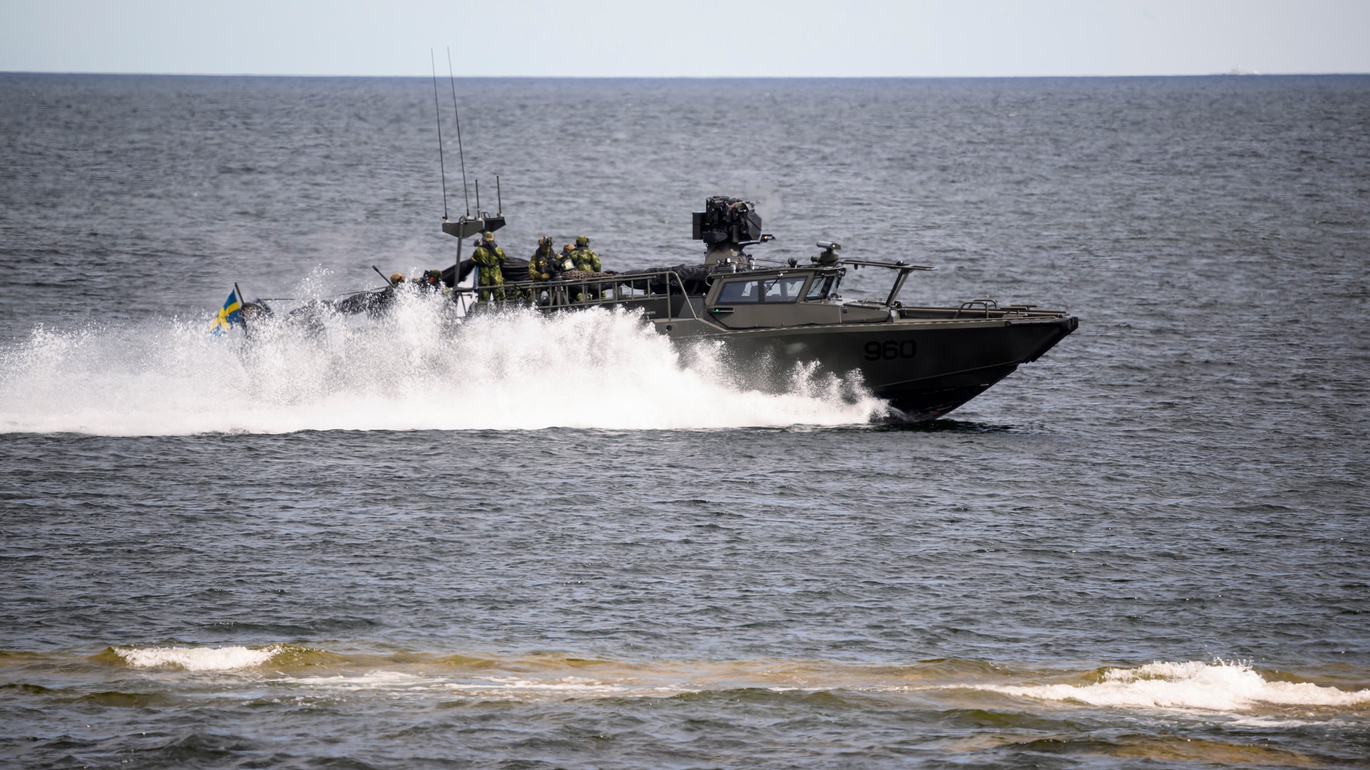 En militär snabbgående båt med soldater ombord kör genom havet och skapar stora vattenstänk.