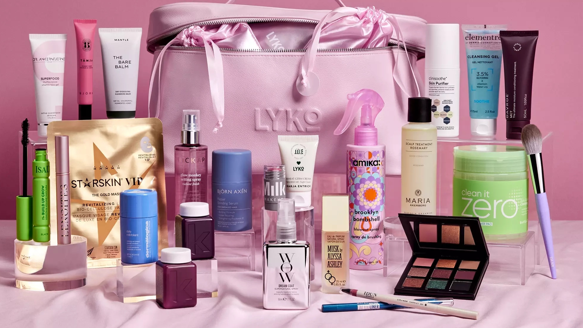 Rosa sminkväska från Lyko omgiven av skönhetsprodukter som krämer, serum, parfym och sminkborstar.