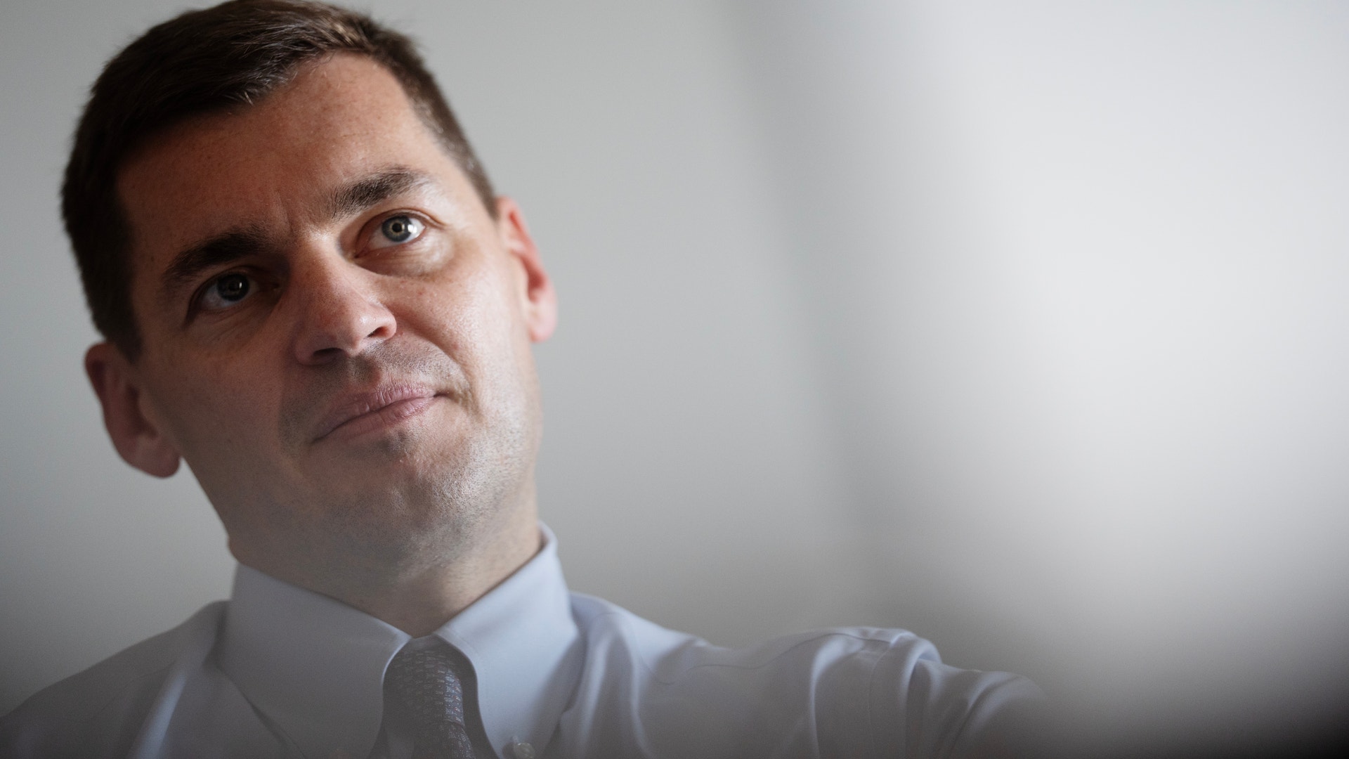 Porträtt av en man i vit skjorta och slips mot neutral bakgrund.
