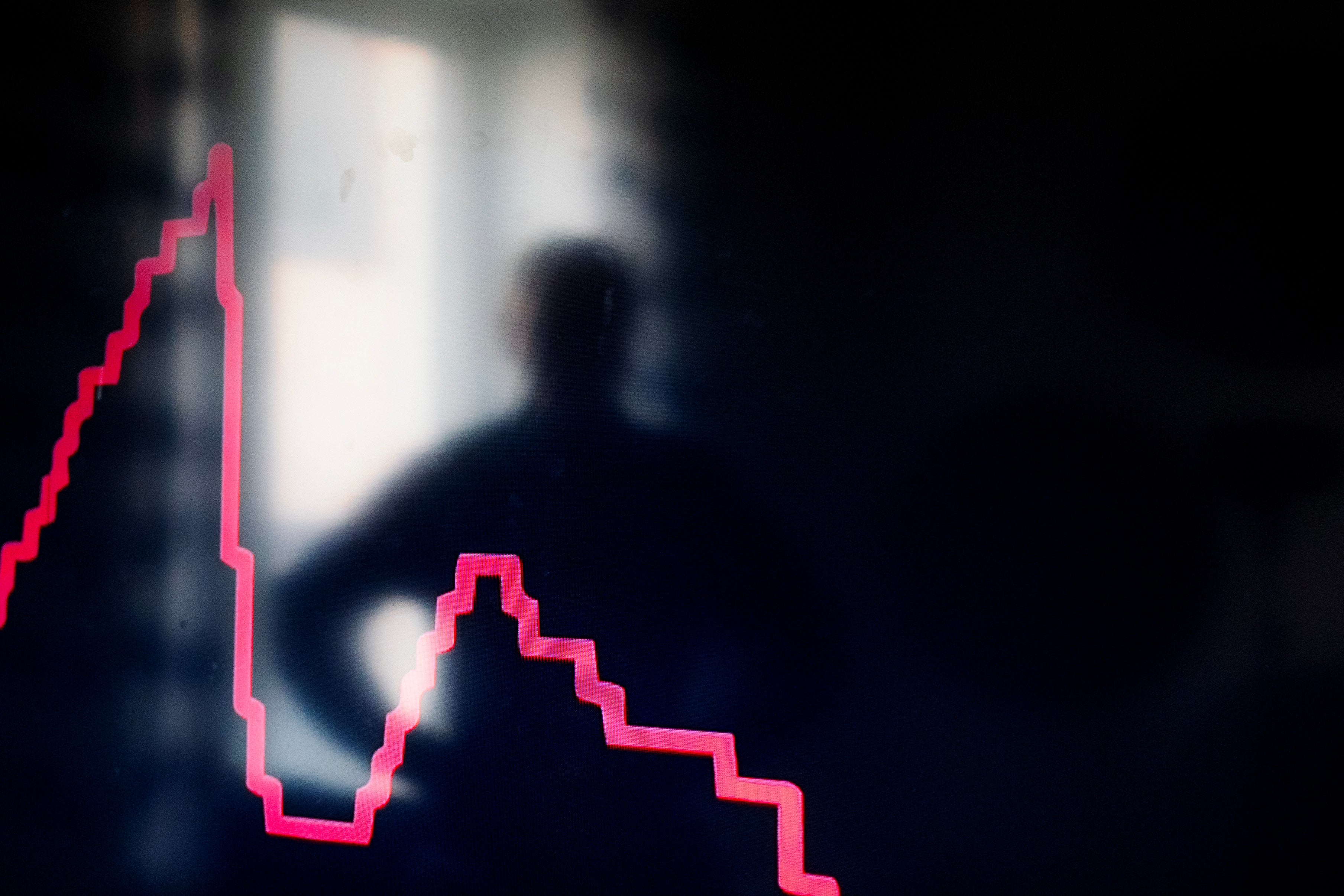 Neonröd graf som visar en fallande trend mot mörk bakgrund med en person i bakgrunden.