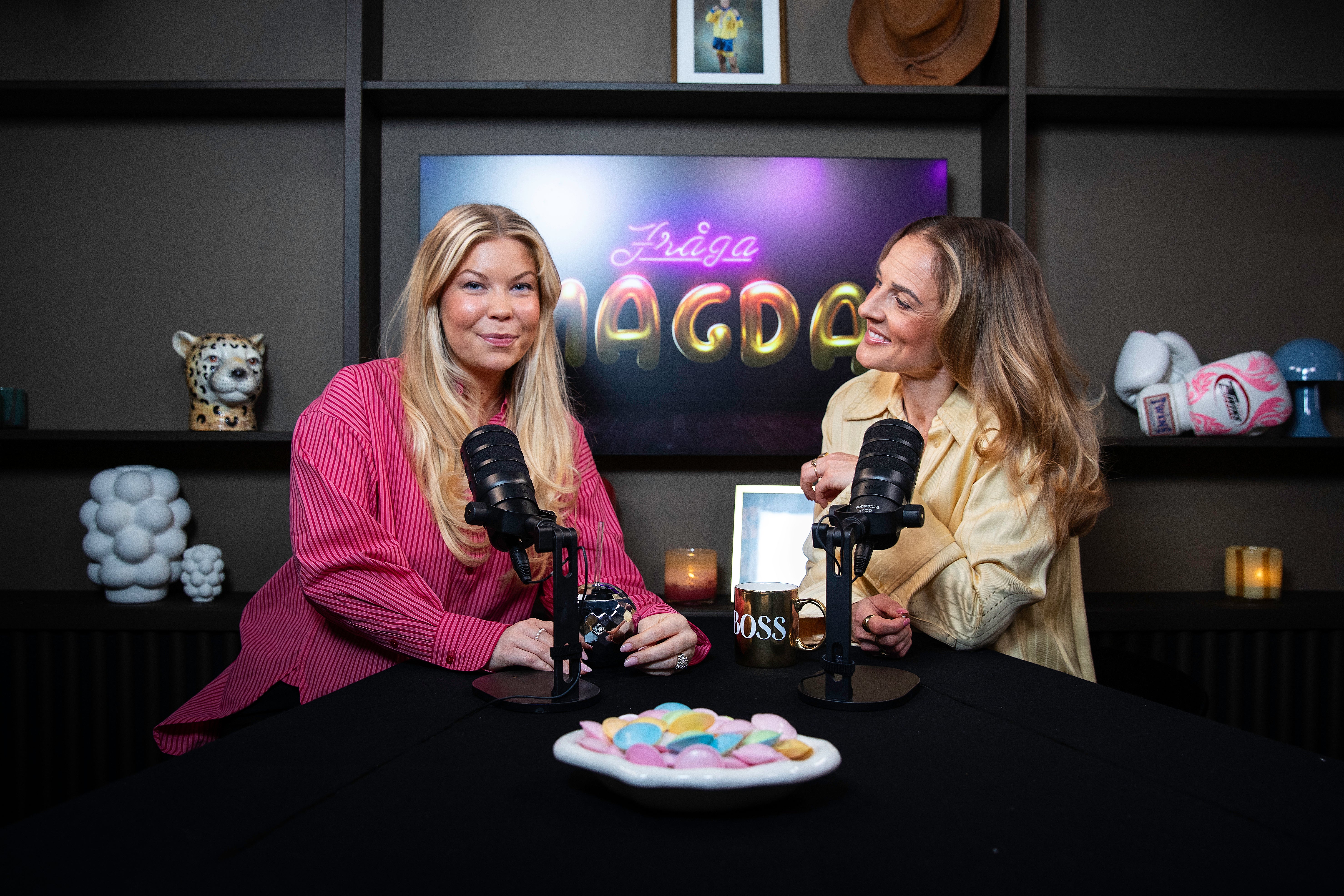 Två kvinnor sitter vid ett bord med mikrofoner under en podcast-inspelning.
