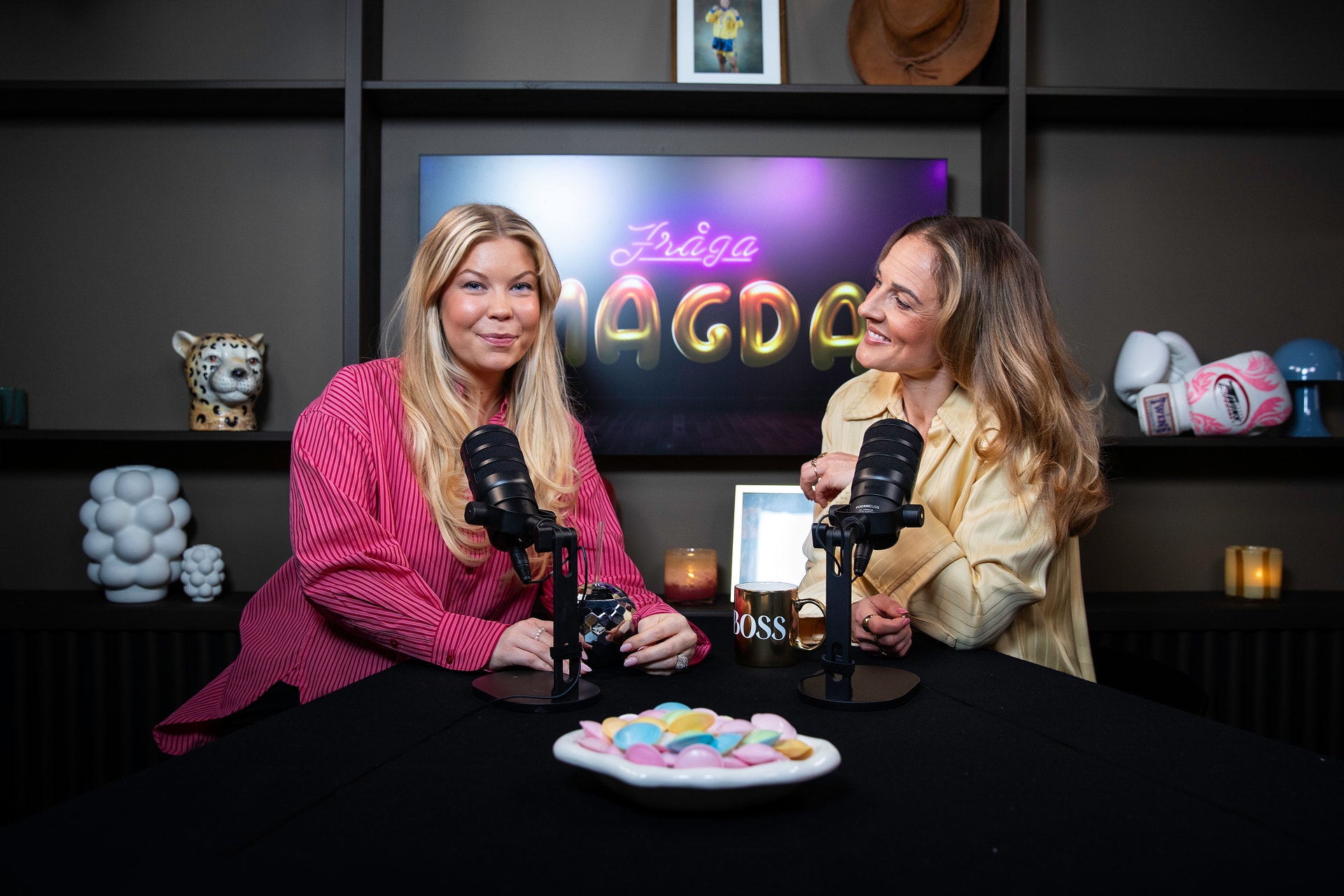 Två kvinnor sitter vid ett bord med mikrofoner under en podcast-inspelning.