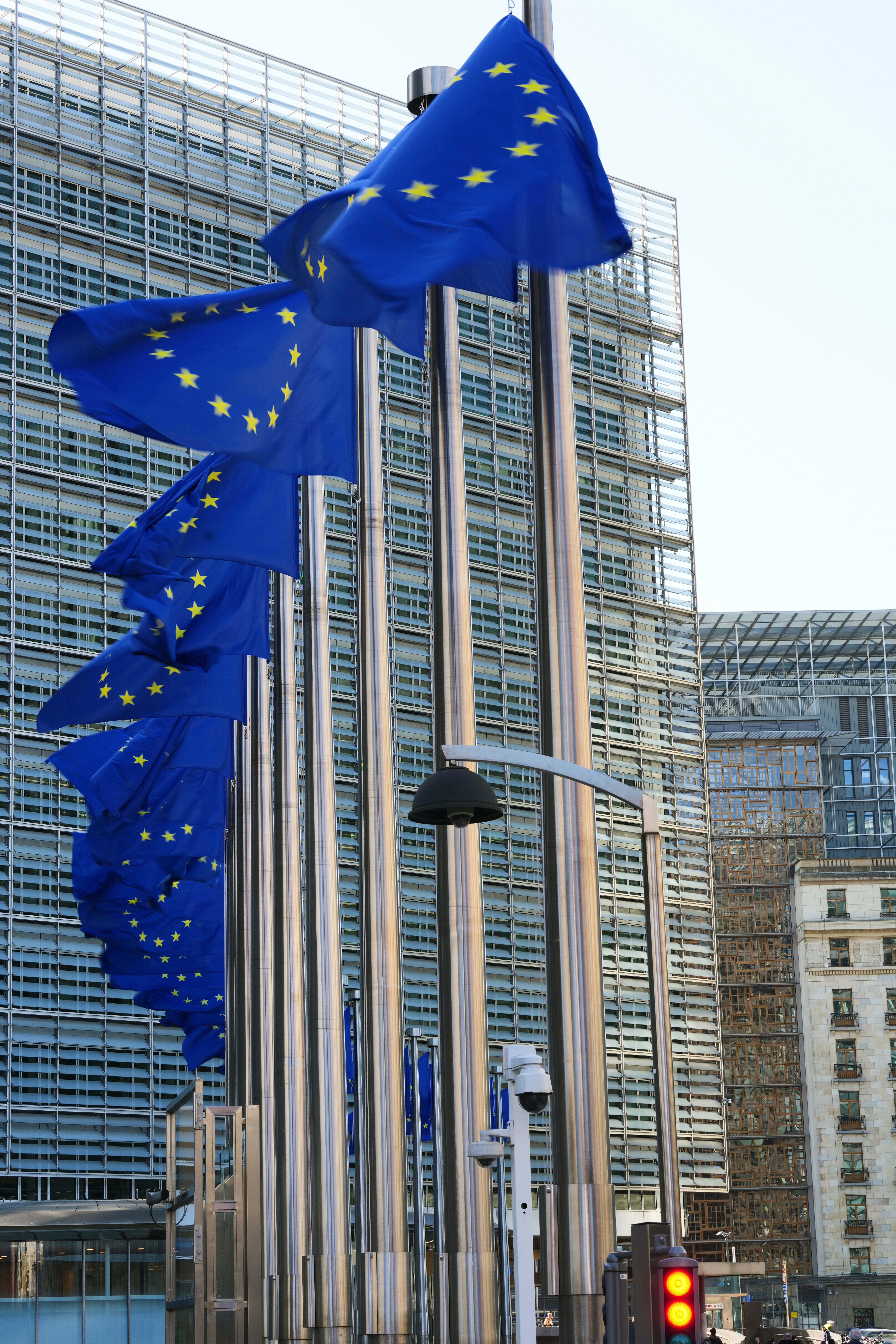 Tre EU-flaggor med blå bakgrund och gula stjärnor som hänger framför moderna kontorsbyggnader.