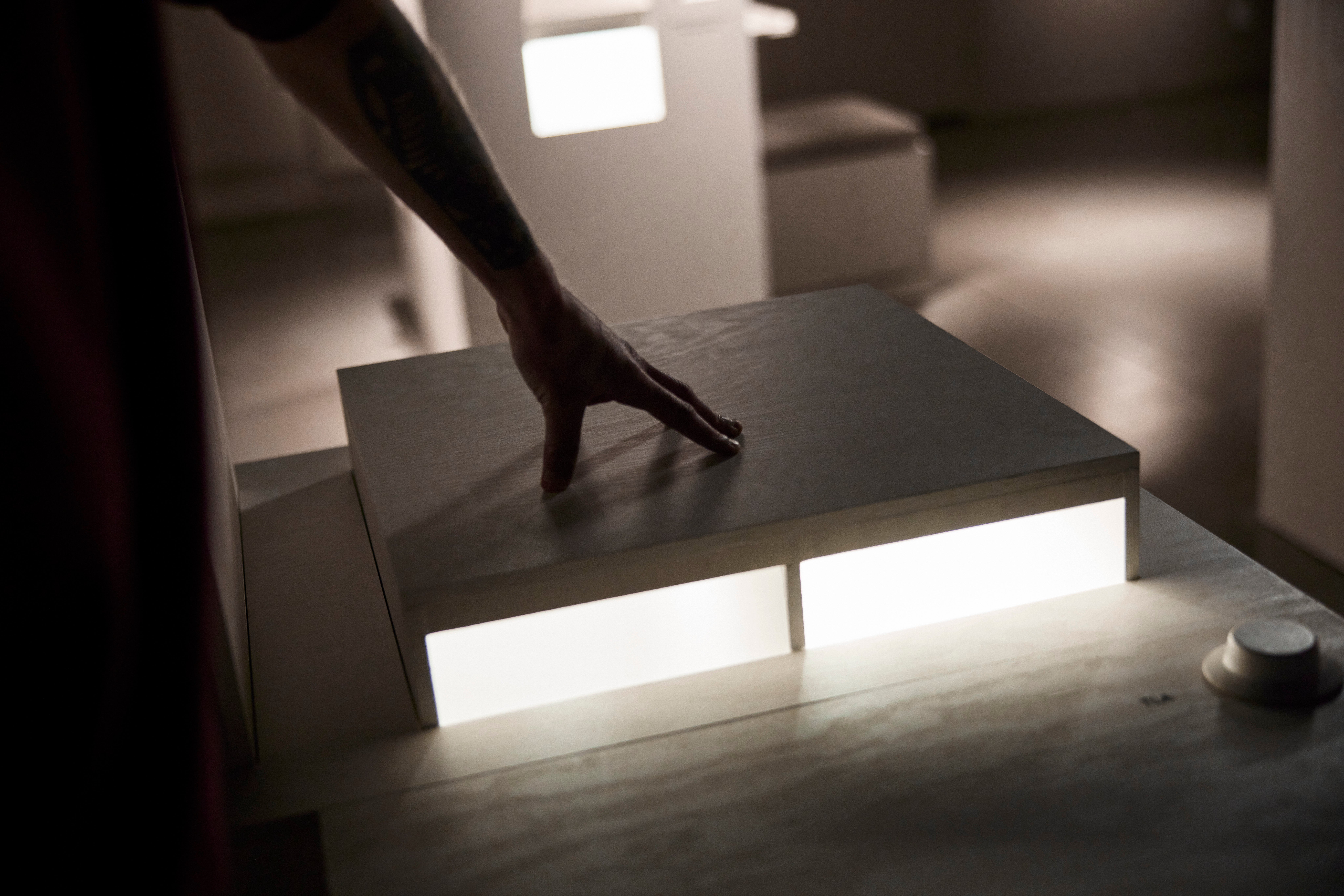 En hand vidrör en modern svart bord med integrerad vit belysning i ett minimalistiskt interiör.